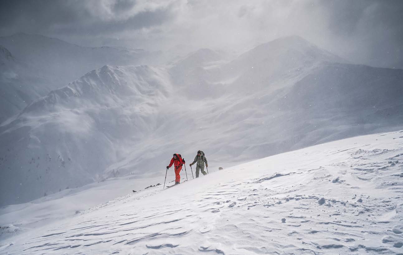 Zwei Skitourengeher im Aufstieg bei Schneetreiben und diffusem Licht