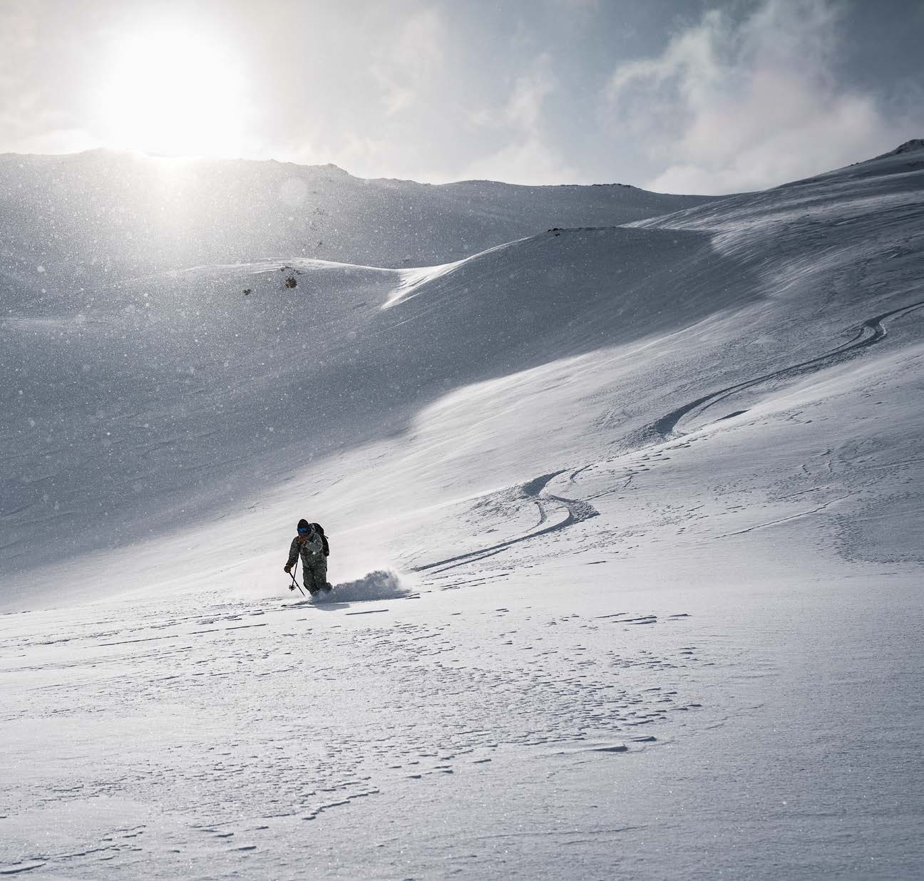 Skifahrer im Gegenlicht auf einem weiten Hang mit Abfahrtsspur
