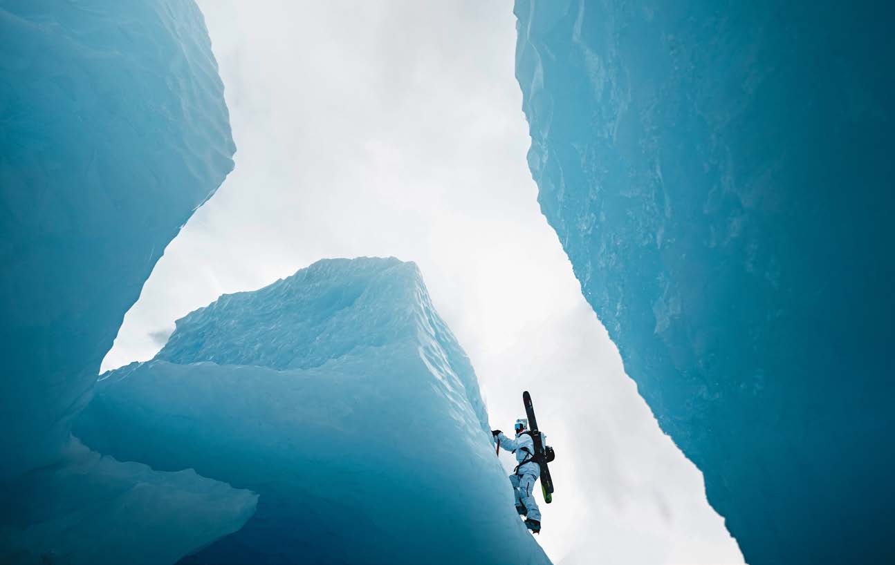 Skifahrer mit Ski auf dem Rucksack steigt zwischen hohen türkisblauen Eiswänden des Sheridan Glacier auf