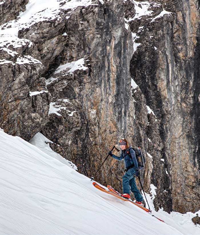 Skitourengeherin steigt am Fuß einer steilen Kalkfelswand im Couloir auf
