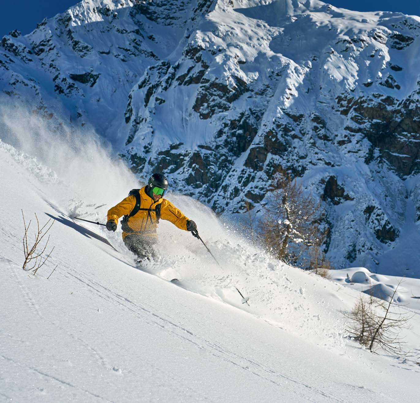 Skifahrer in gelber Jacke im Pulverschnee unter steilen verschneiten Felswänden