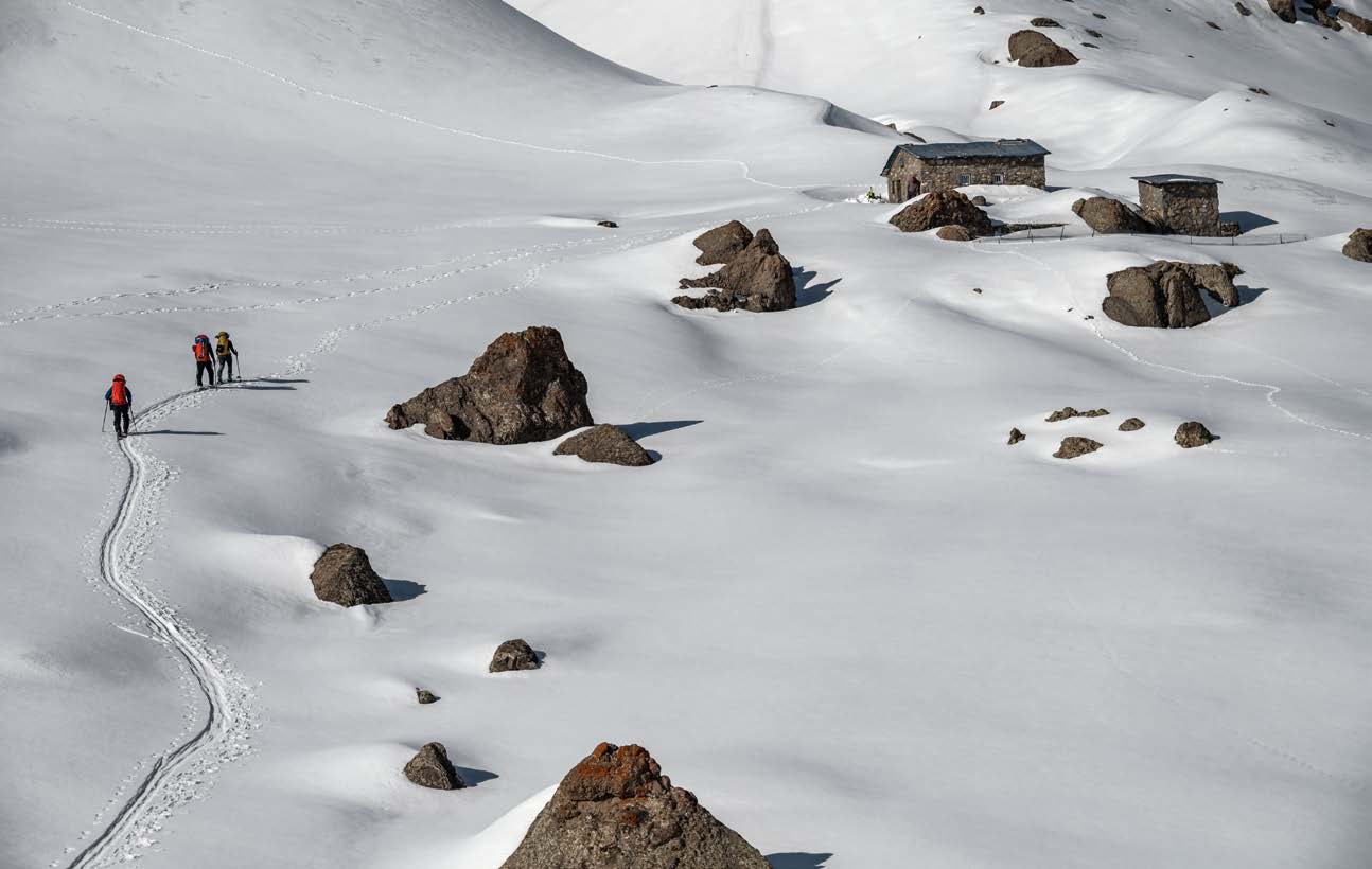 Ski touring group setting a track between boulders toward a stone hut