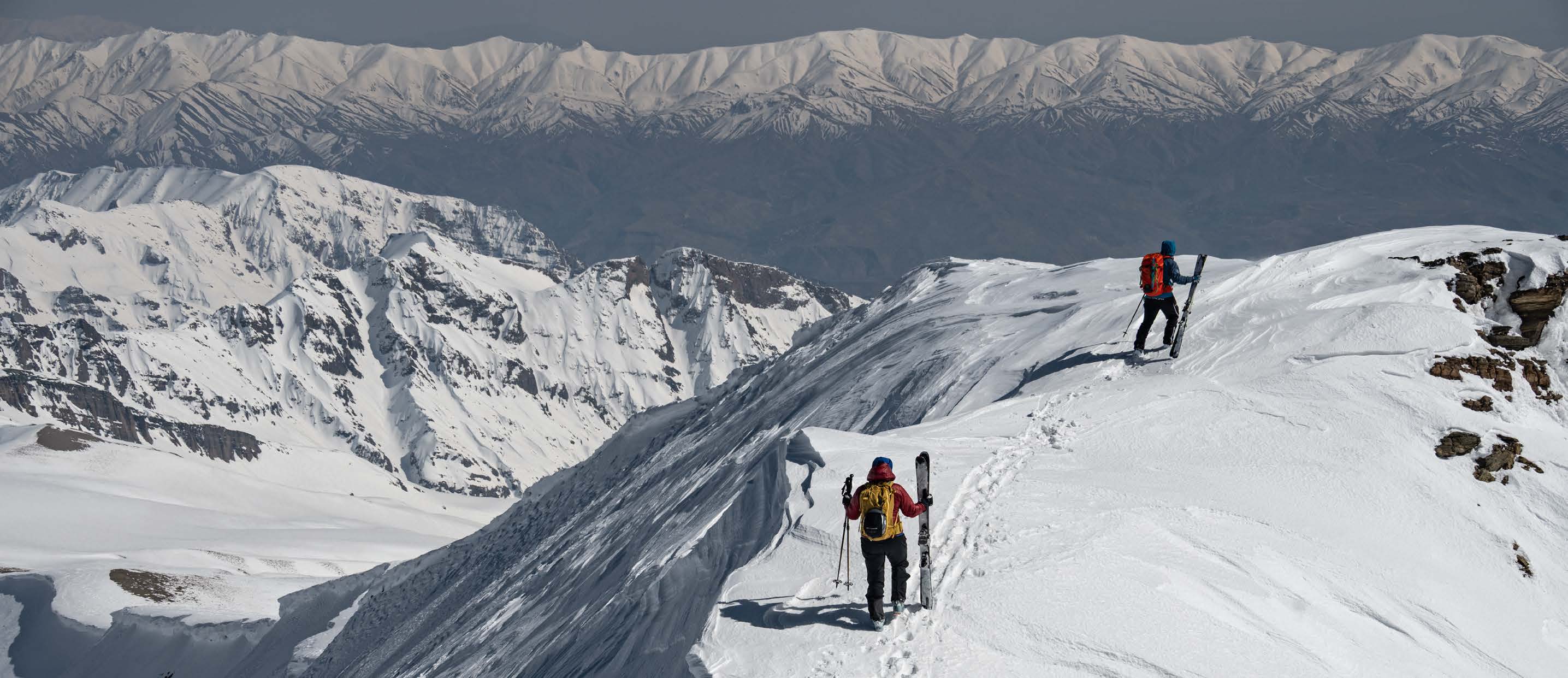 Ski tourers on a snowy ridge above hazy valleys in Iran