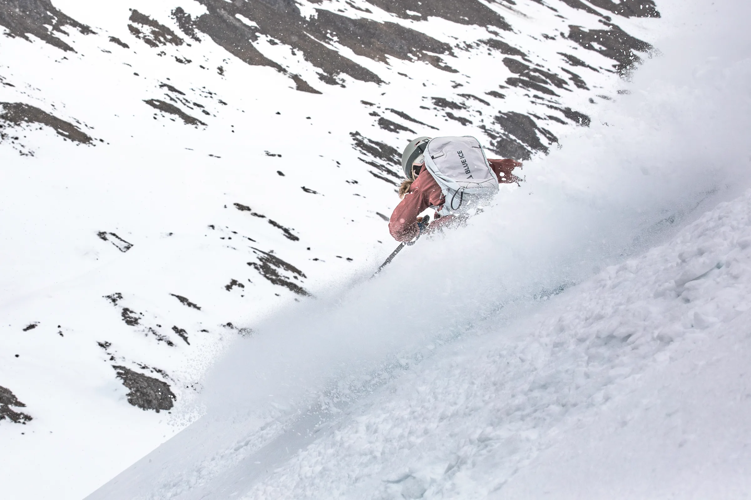 Rear view of Andrea Limbacher skiing powder beneath snow-covered rocky slopes in Lenzerheide.