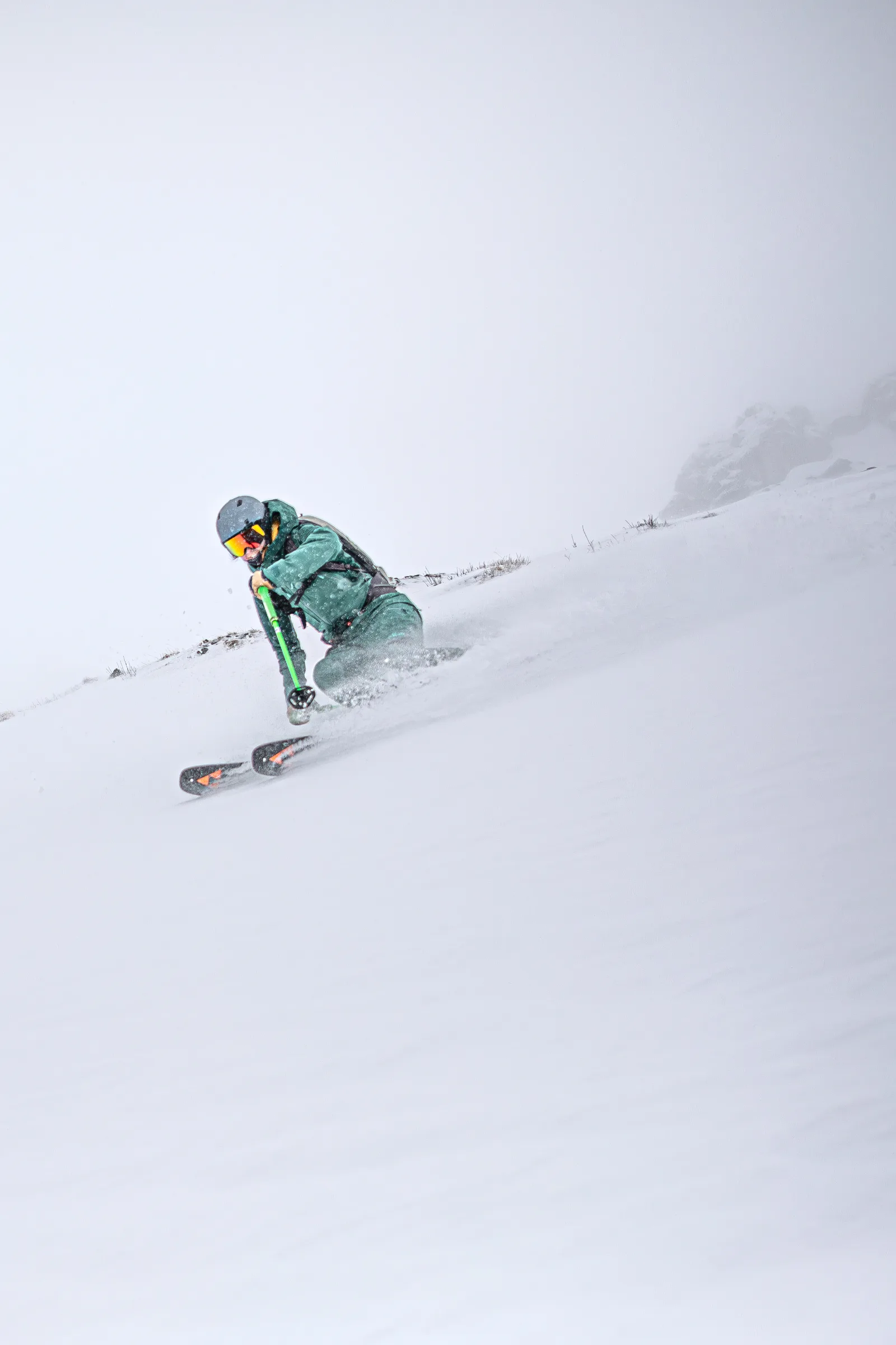 Annika Schlachter skis in a low crouch through snow on a misty slope in Gastein, wearing green ski clothing, with rocks emerging behind her.