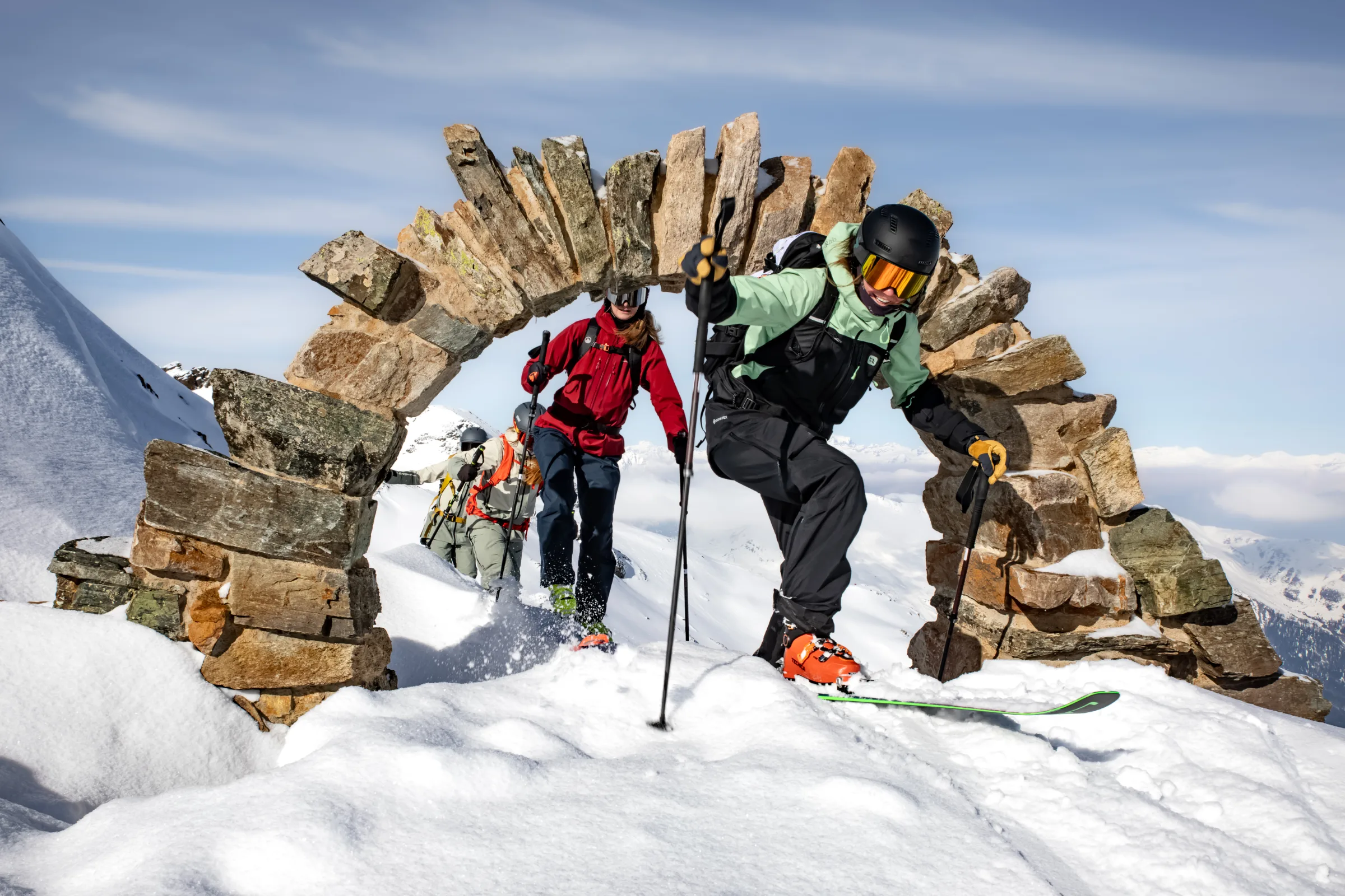 Annika Schlachter moves on skis through a stone arch in the snow at Lenzerheide, followed by others in ski gear.