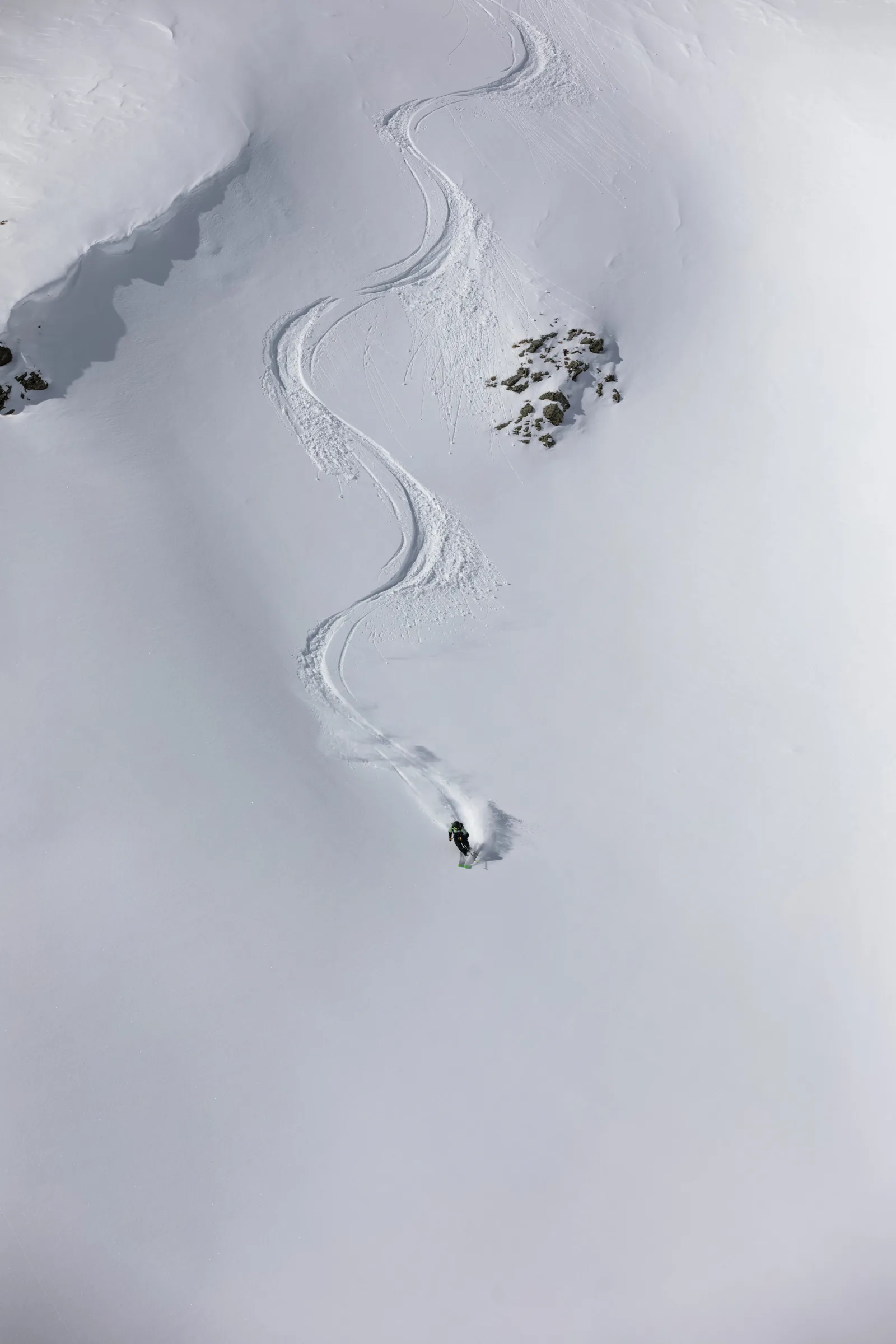 Annika Schlachter makes a turn on a broad powder slope, her S-shaped tracks winding down from high above between exposed rocks.