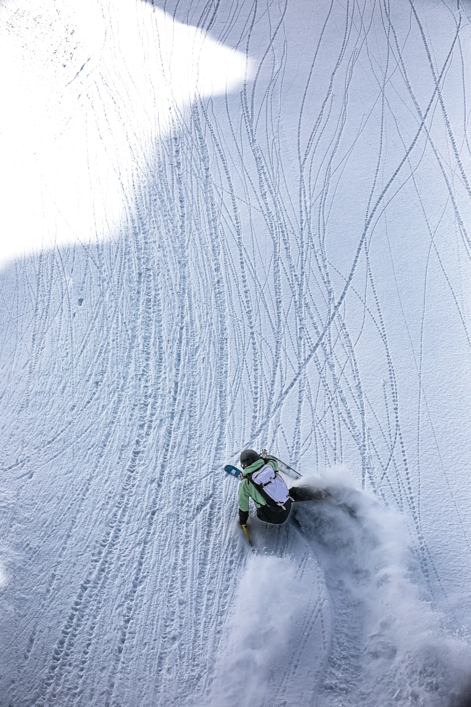 Seen from behind, Annika Schlachter leans low into a ski turn, throwing up snow on a slope covered in fine tracks.