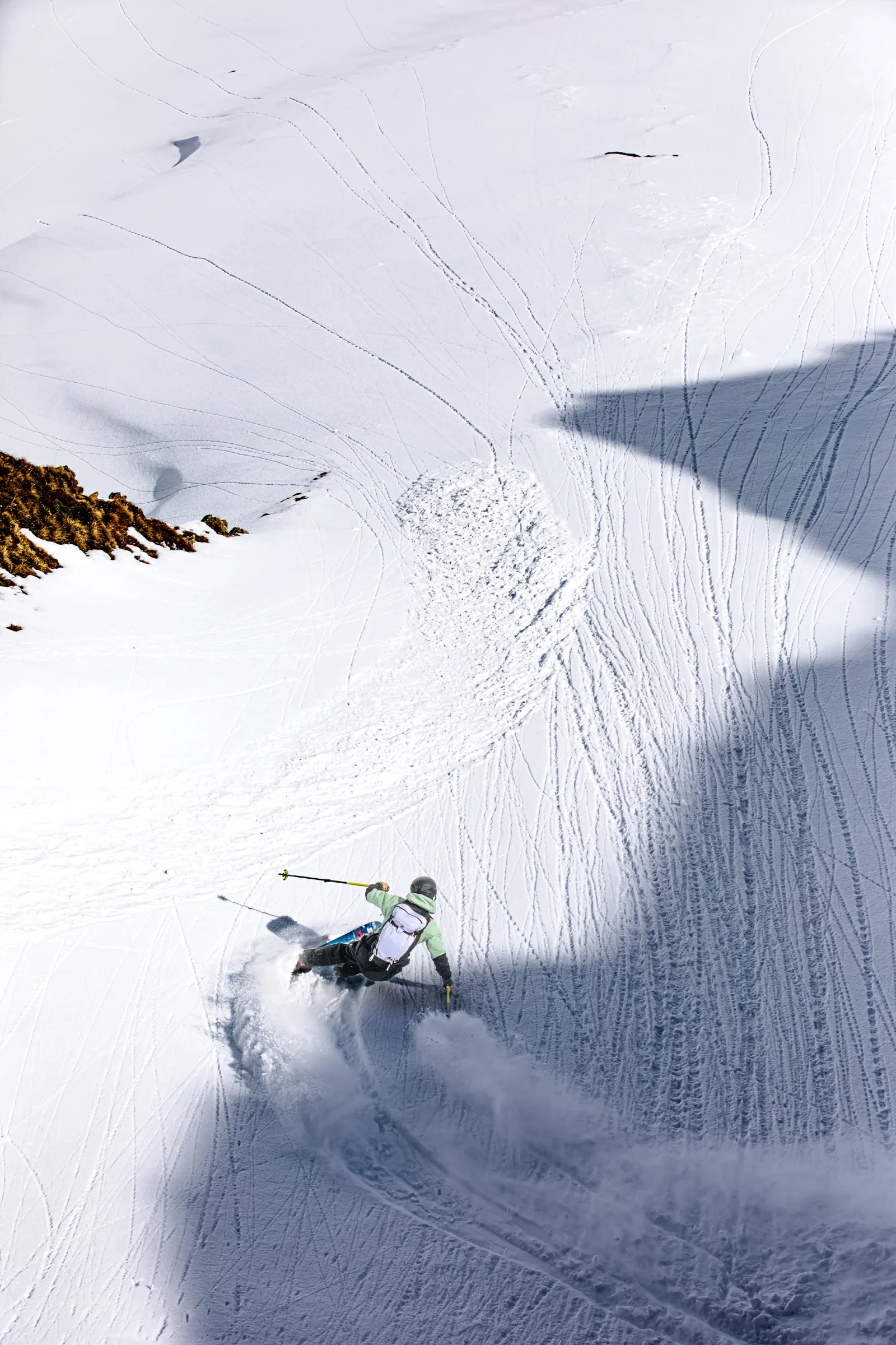 Annika Schlachter turns with her poles spread at the edge of sun and shade, with brown grass exposed above her on the snowy slope.