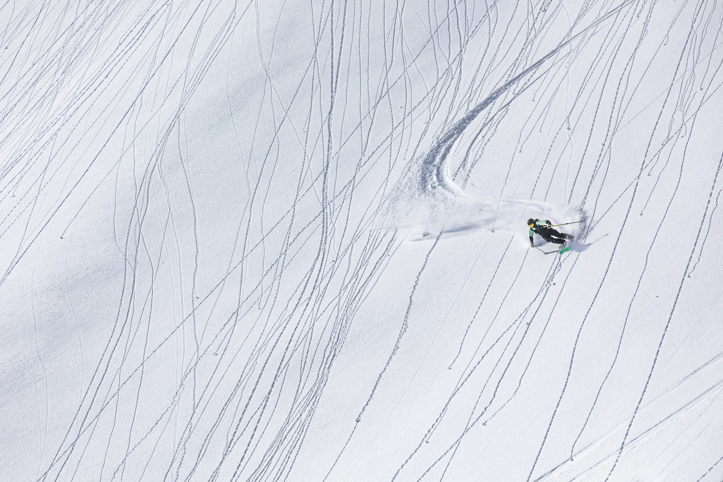 Annika Schlachter leans into a turn on a broad snowy slope lined with fine tracks, leaving a wide arc and a spray of snow behind her.