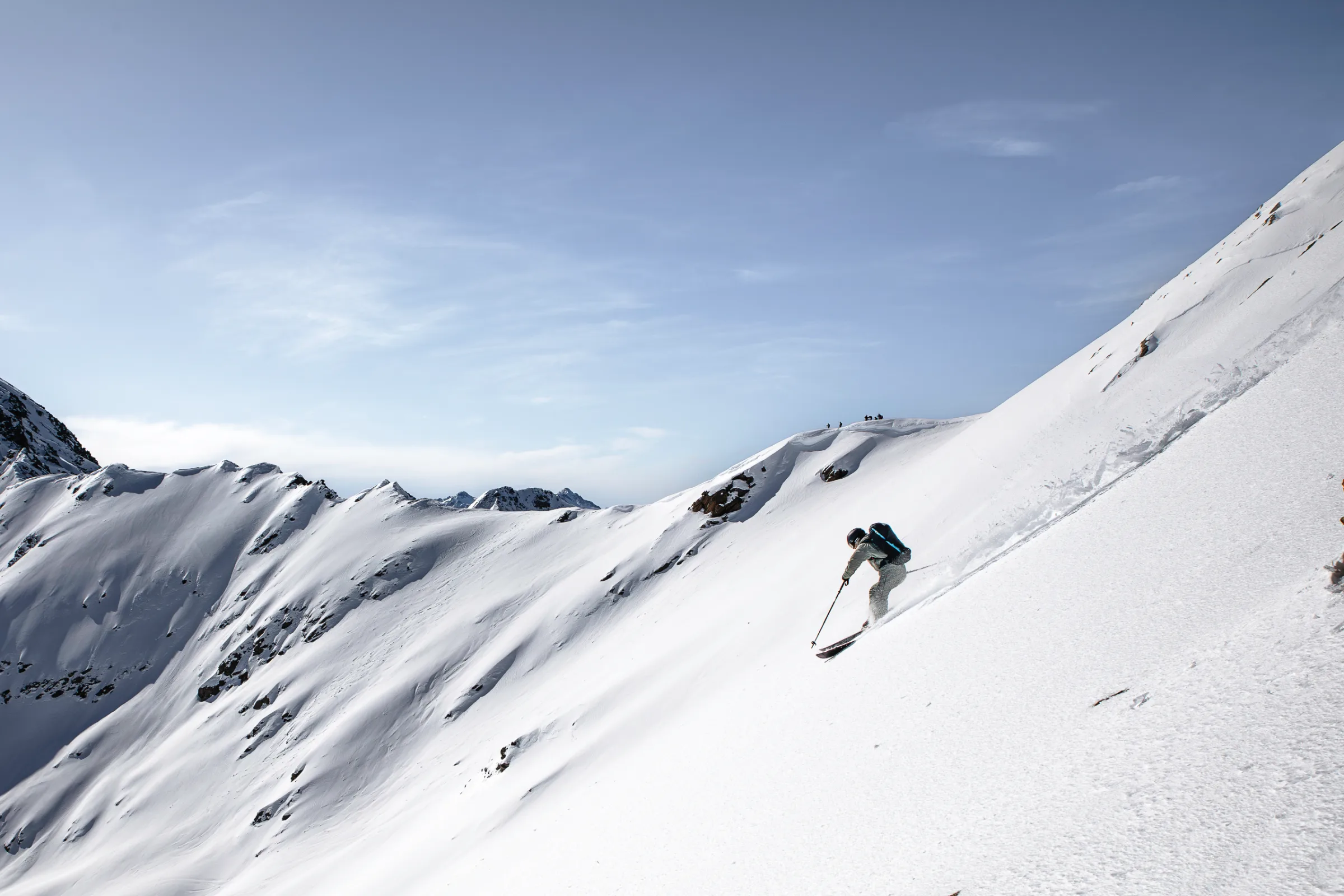 Bernd Hassmann skis down a steep, open snow slope near Lenzerheide with a backpack, surrounded by rocky, snow-covered ridges.