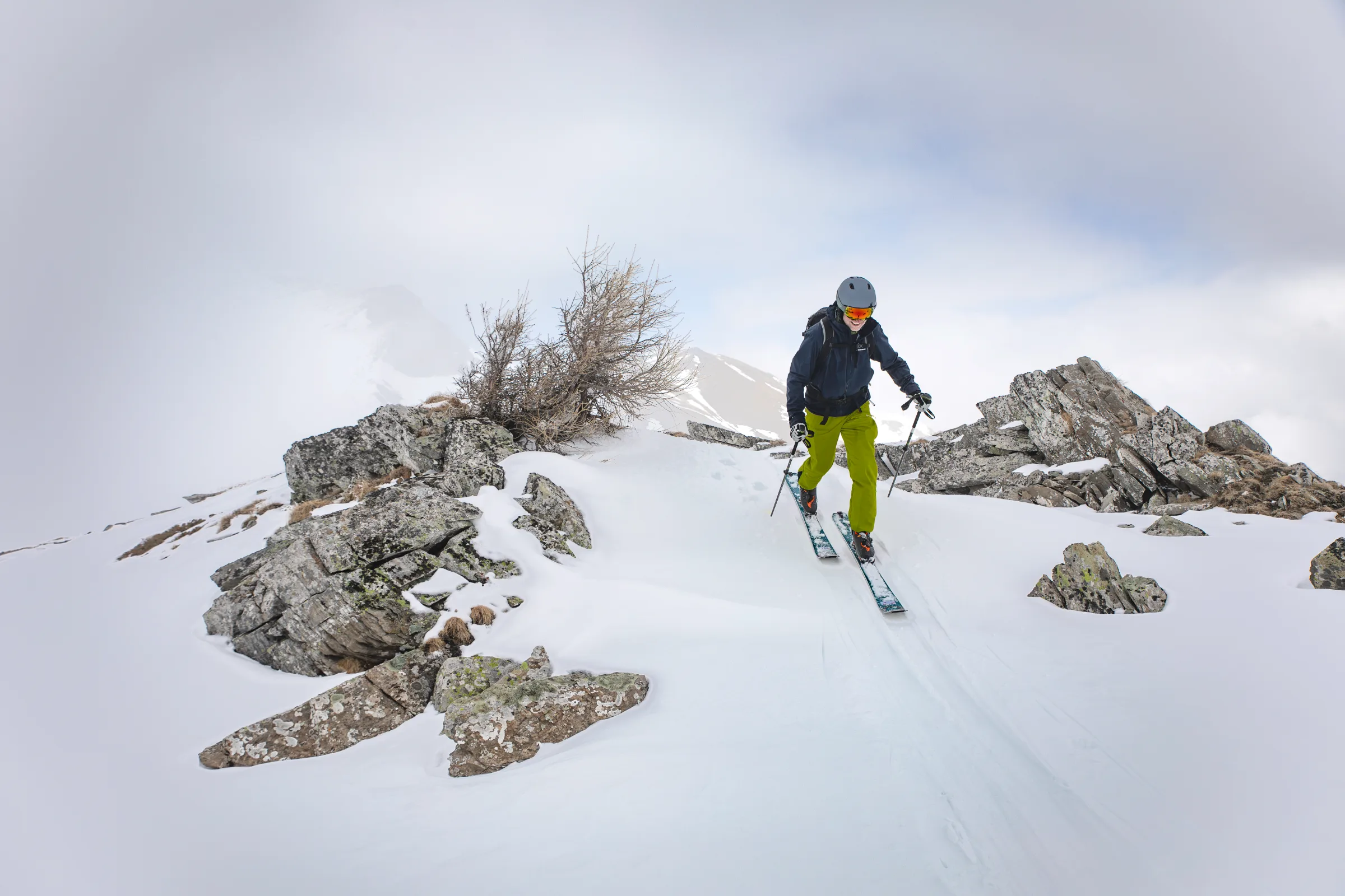 Christoph Öfele bewegt sich mit Ski und Stöcken über einen verschneiten, felsigen Grat, hinter dem Berggipfel im Nebel verschwinden.