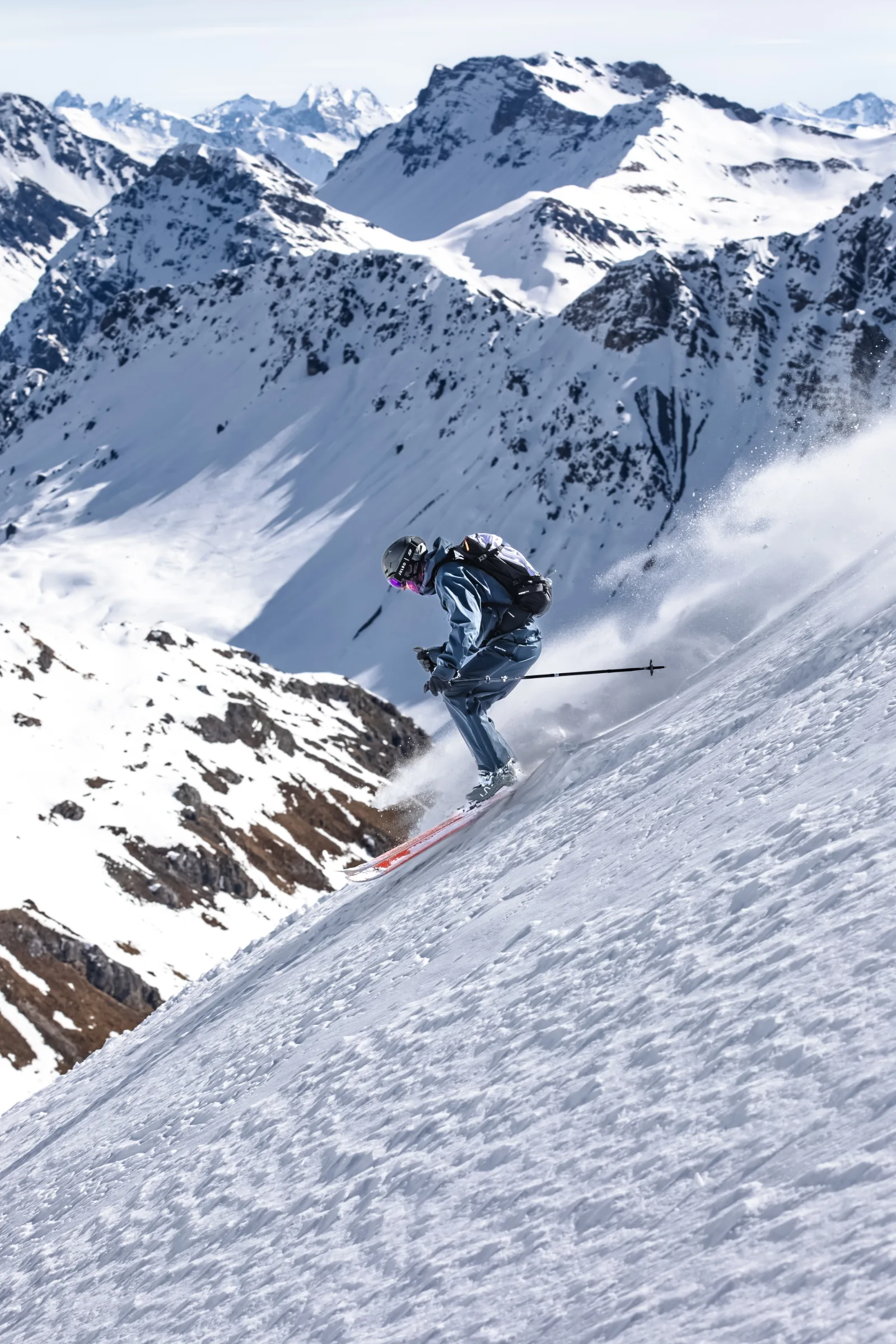 Christoph Öfele fährt mit gebeugten Knien und Rucksack über einen steilen Schneehang vor einem Panorama schneebedeckter Felsgipfel.