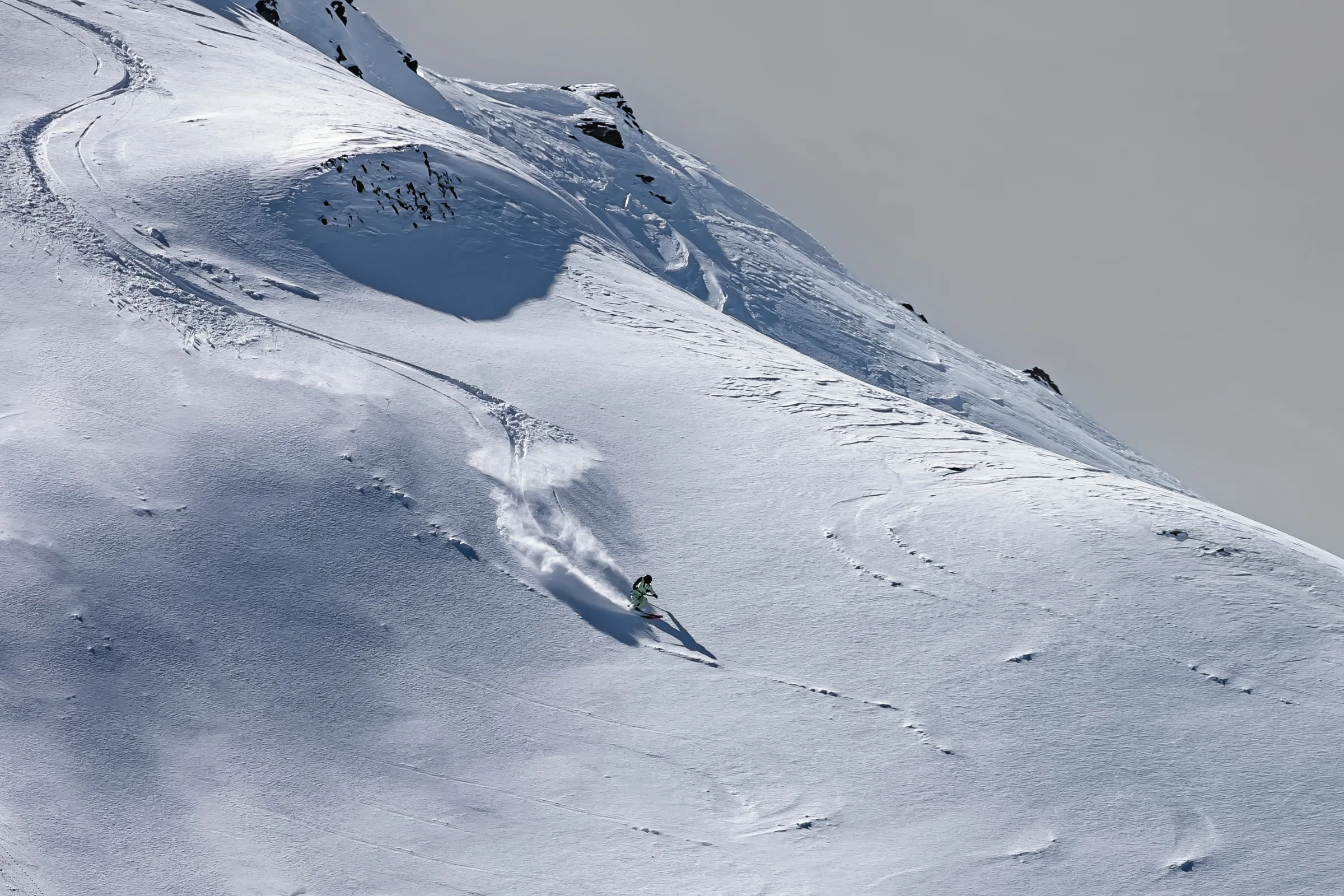 Claudia Kohler skis across a broad slope below snow-covered rock formations, leaving a curved track in the snow.