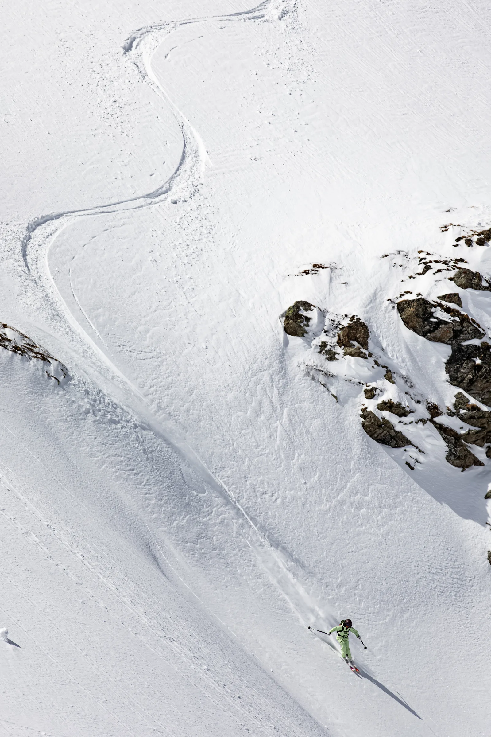 Claudia Kohler skis down a steep snowy slope in Lenzerheide in light green clothing, with winding ski tracks behind her and snow-covered rocks to the right.