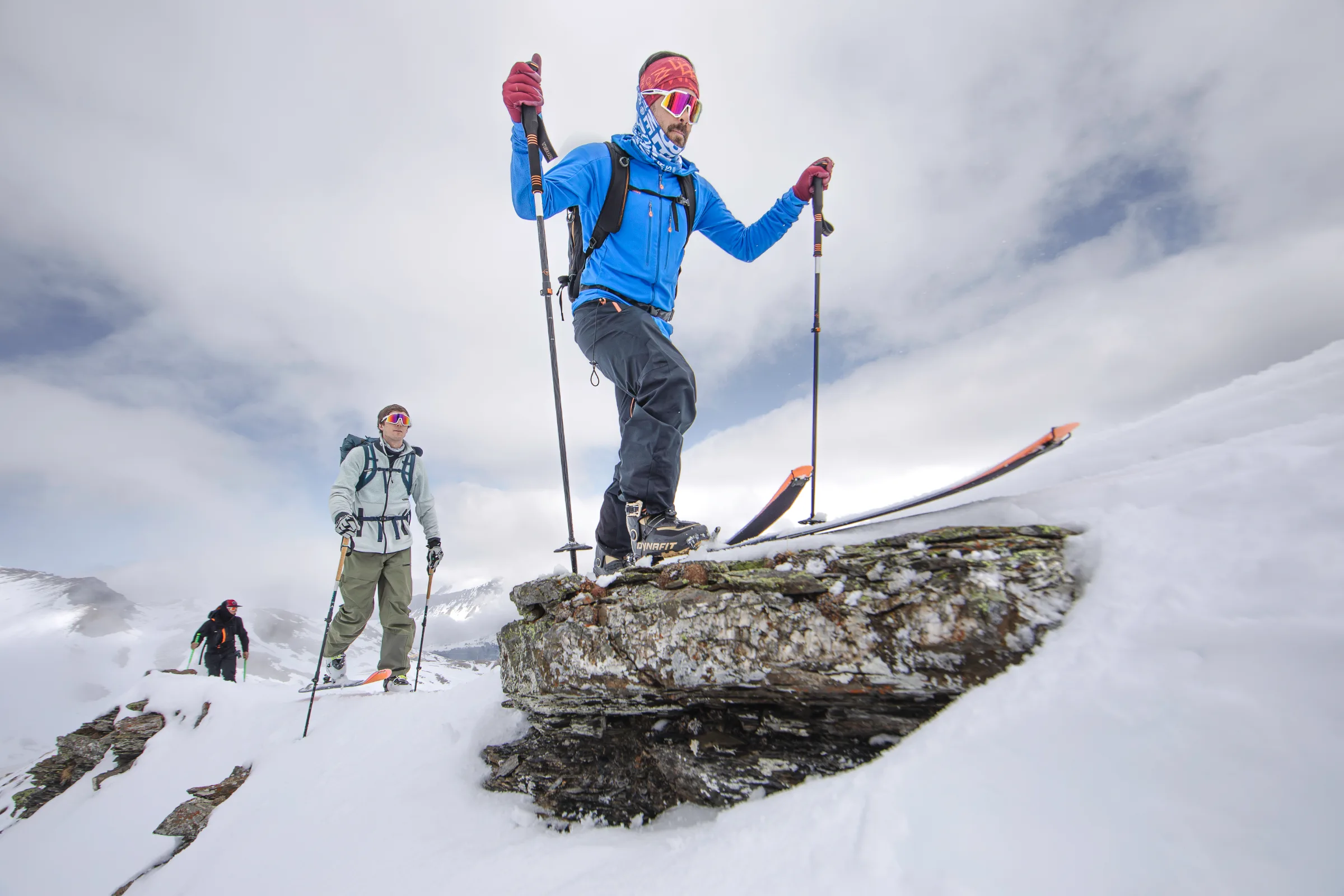 Florian Eigler climbs a snowy rock step on touring skis near Lenzerheide in a blue jacket, with two other people following.