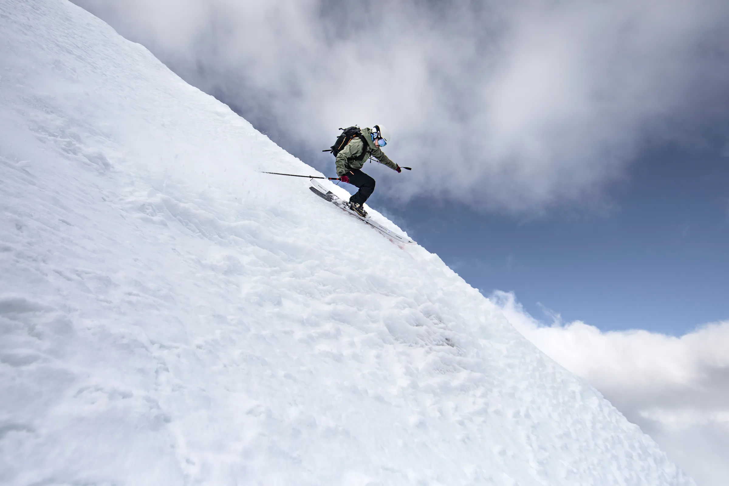 Florian Eigler skis down a steep snowy slope with bent knees against a sky of blue patches and thick clouds.