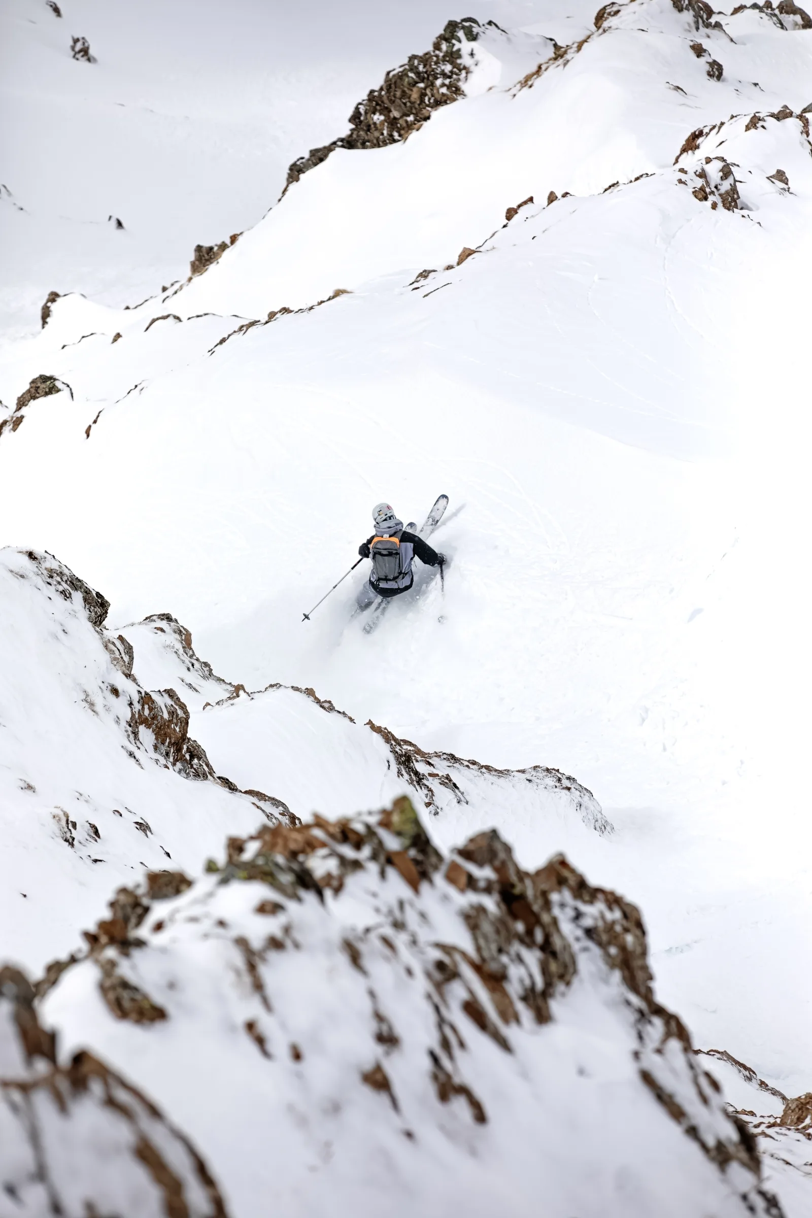 Seen from behind, Florian Eigler skis through deep snow between rugged rocks in Lenzerheide, wearing a helmet and backpack.
