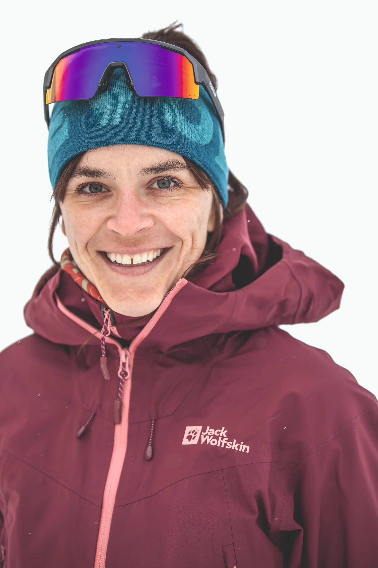 Martina Wengenmeir lächelt vor weißem Hintergrund in die Kamera, mit türkisfarbenem Stirnband, verspiegelter Sonnenbrille auf dem Kopf und burgunderroter Jacke.