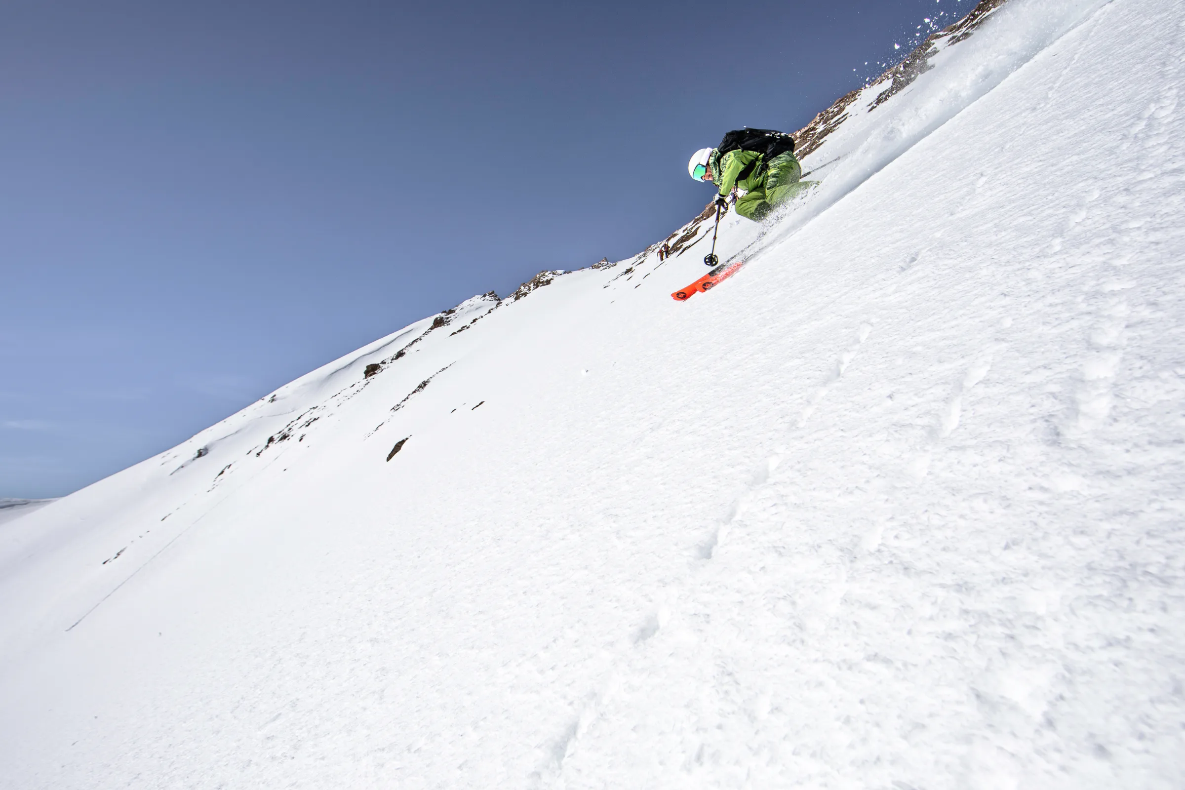Martina Wengenmeir fährt in tiefer Haltung einen steilen Schneehang unter blauem Himmel hinab und wirbelt mit ihren Ski Schnee auf.