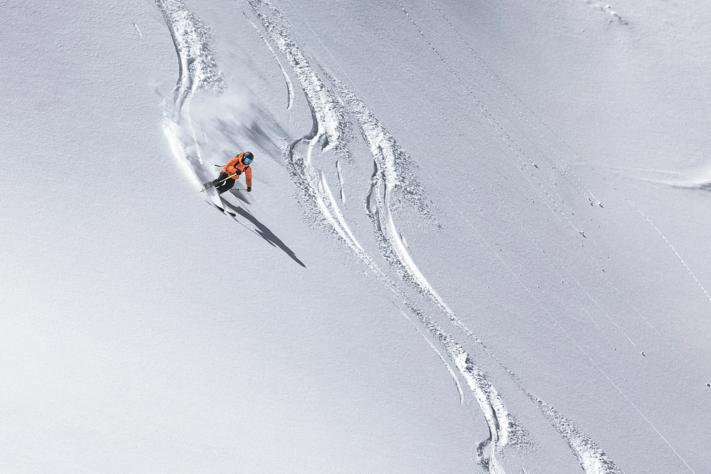Martina Wengenmeir legt sich auf einem weiten Schneehang neben vorhandenen Skispuren in die Kurve und wirbelt Schnee auf; ihr langer Schatten fällt hangabwärts.