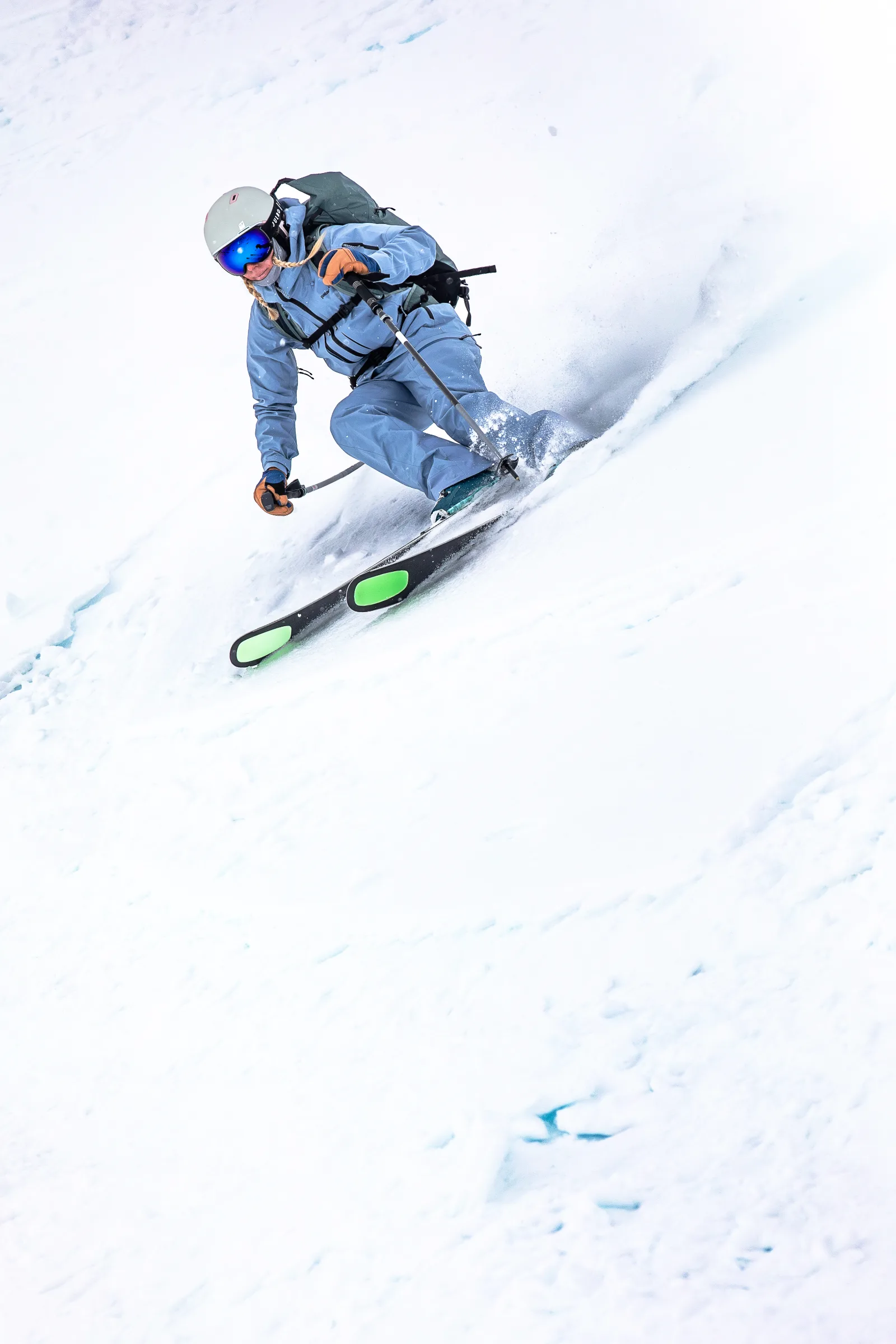 Michaela Casotti leans into a turn on a snowy slope, spraying snow in light blue ski clothing, a helmet and a backpack.