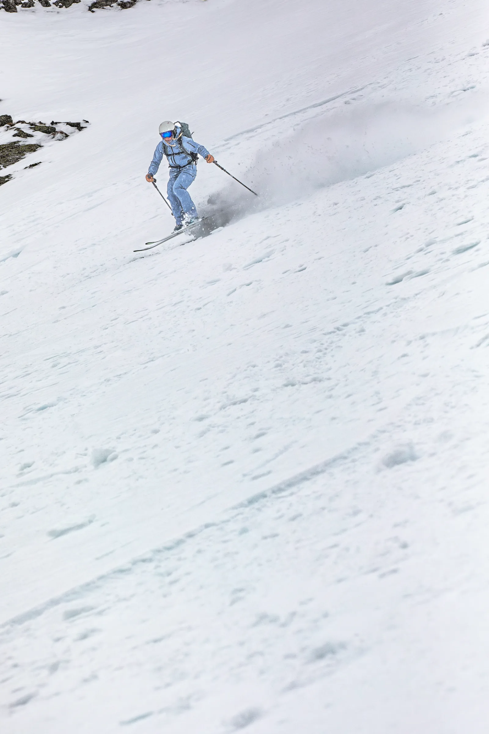 Michaela Casotti skis down a broad snowy slope with her poles held out to the sides, leaving a cloud of snow behind her.