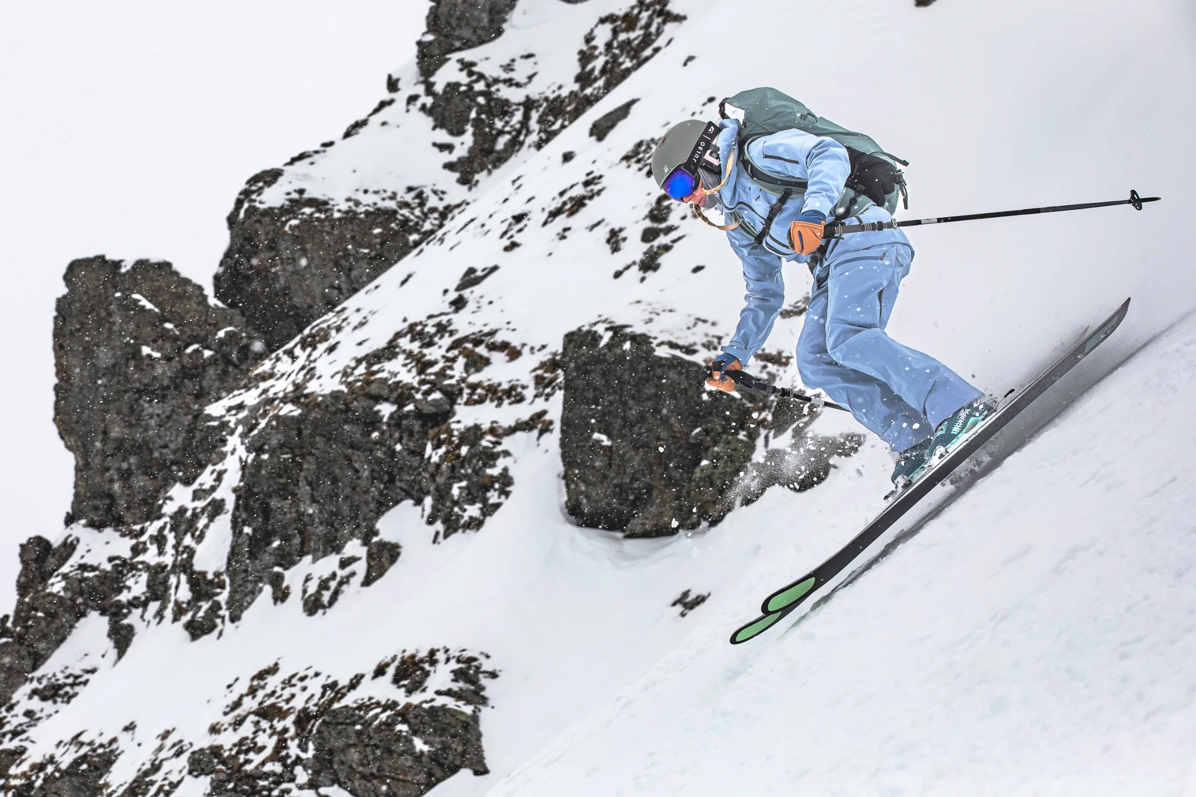 Michaela Casotti leans forward as she skis down a steep snowy slope in front of dark, snow-covered rock faces.