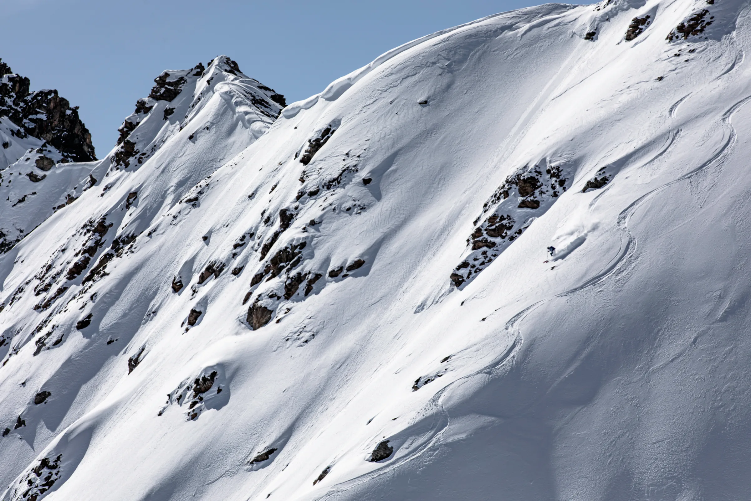 Michaela Casotti skis through powder down a steep, rocky slope in Lenzerheide beside curved ski tracks.