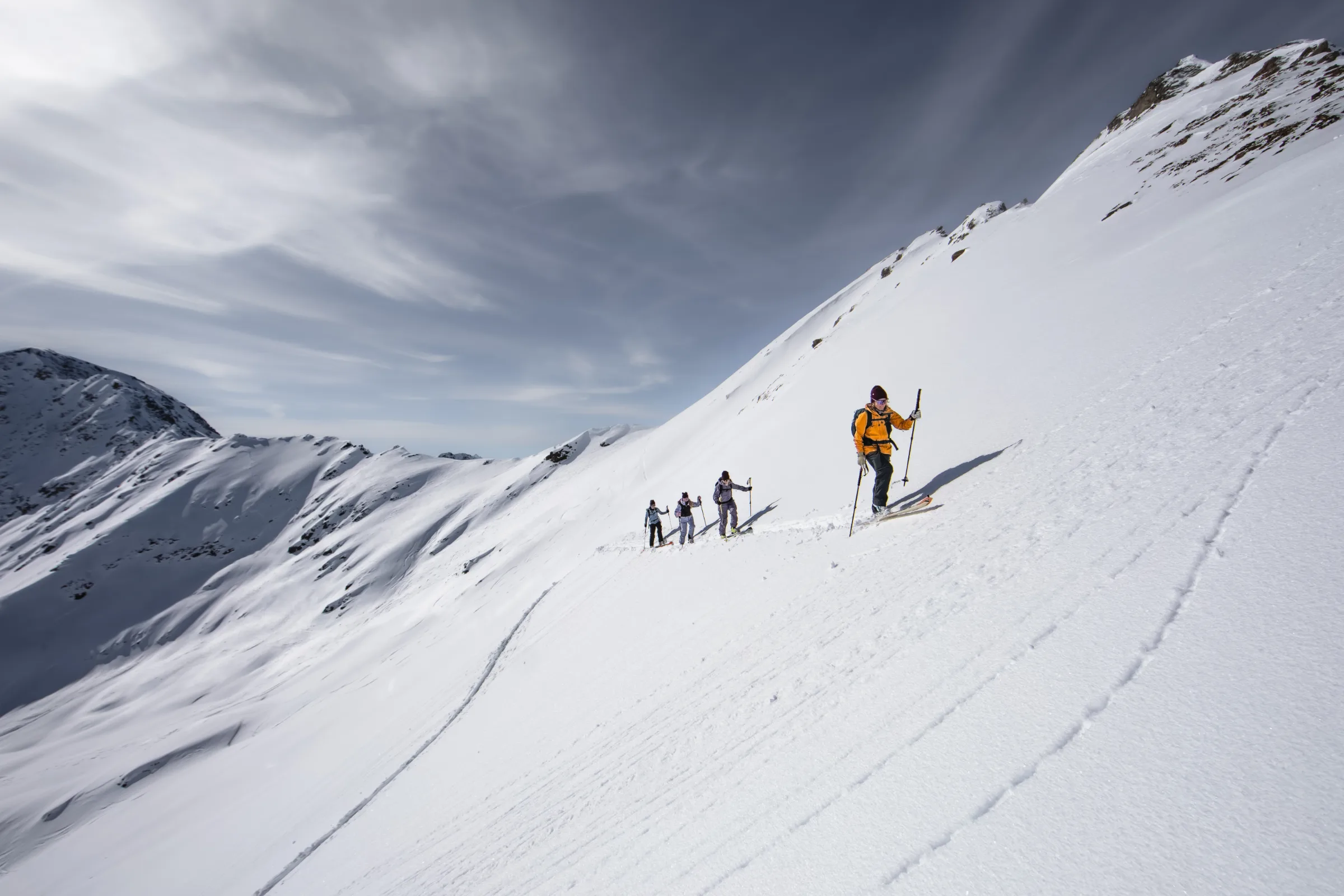 Michaela Casotti, wearing an orange jacket, climbs a steep snowy slope near Lenzerheide ahead of three other ski tourers.
