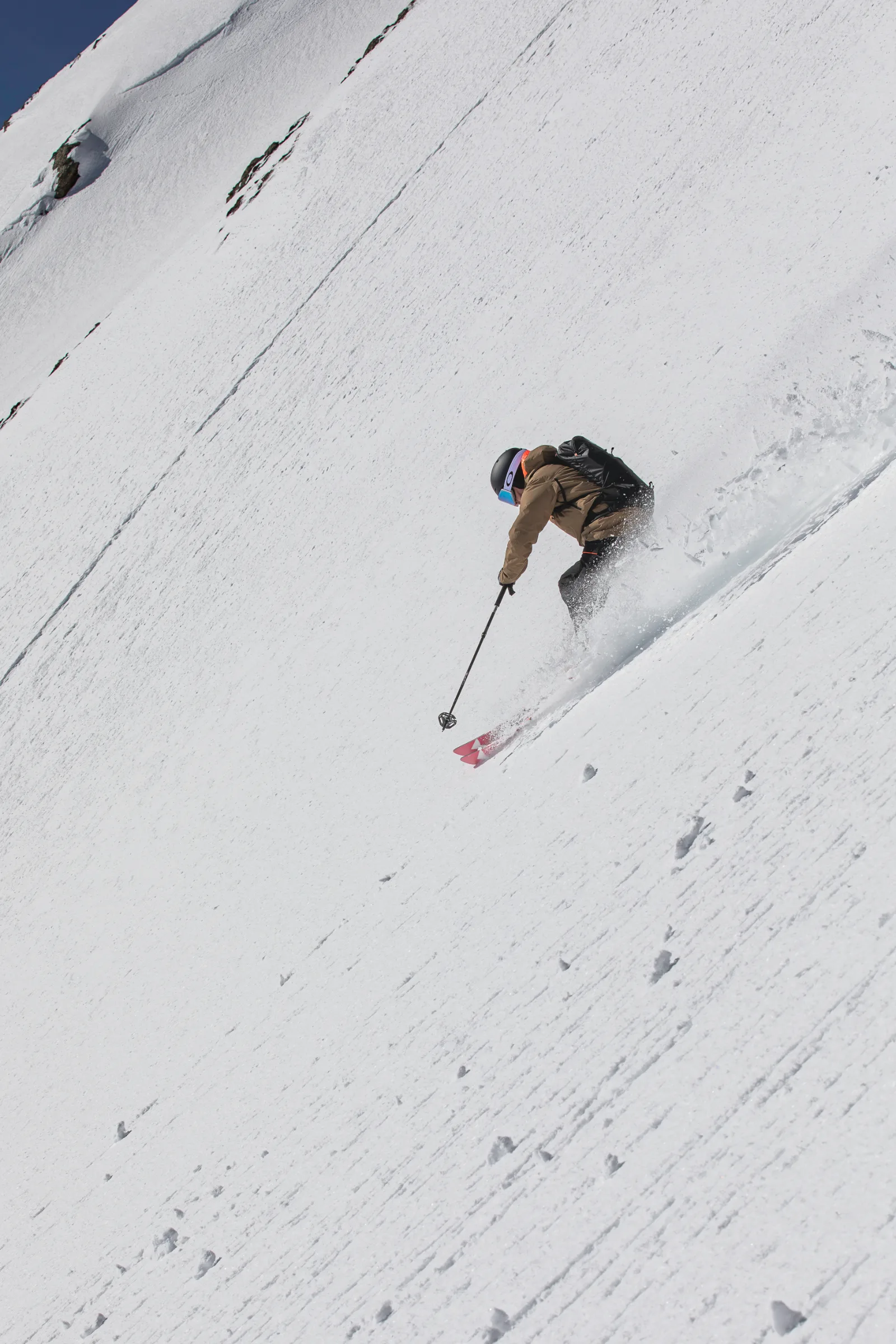 Von hinten gesehen fährt Mico Kehrle mit schwarzem Rucksack einen steilen Schneehang hinab und wirbelt beim Schwung Schnee auf.