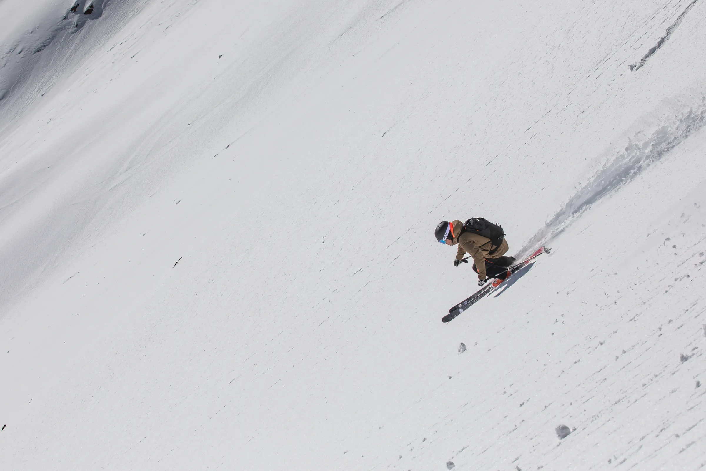 Mico Kehrle fährt in tiefer Hocke mit parallelen Ski quer über einen offenen, steilen Schneehang und zieht eine Spur hinter sich.