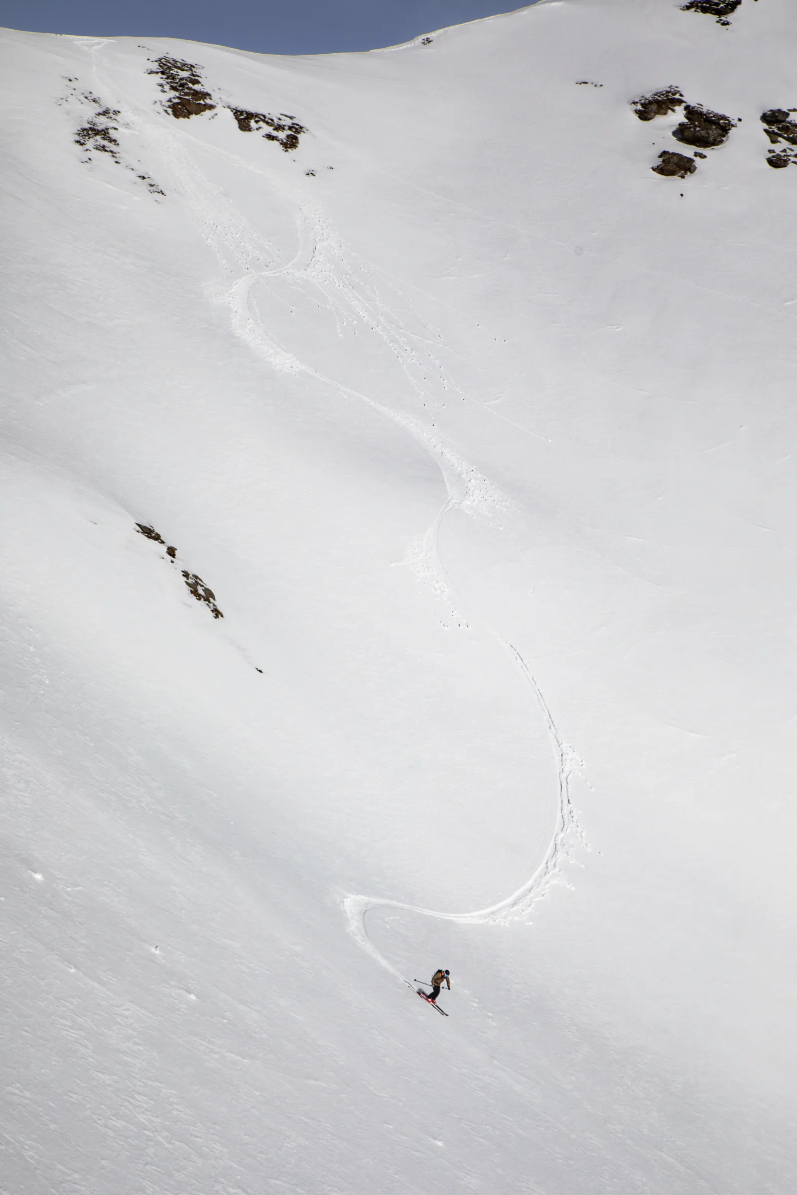 Mico Kehrle ist unten auf einem weiten Schneehang bei Lenzerheide zu sehen; eine lange geschwungene Skispur führt von den Felsen oberhalb zu ihm.