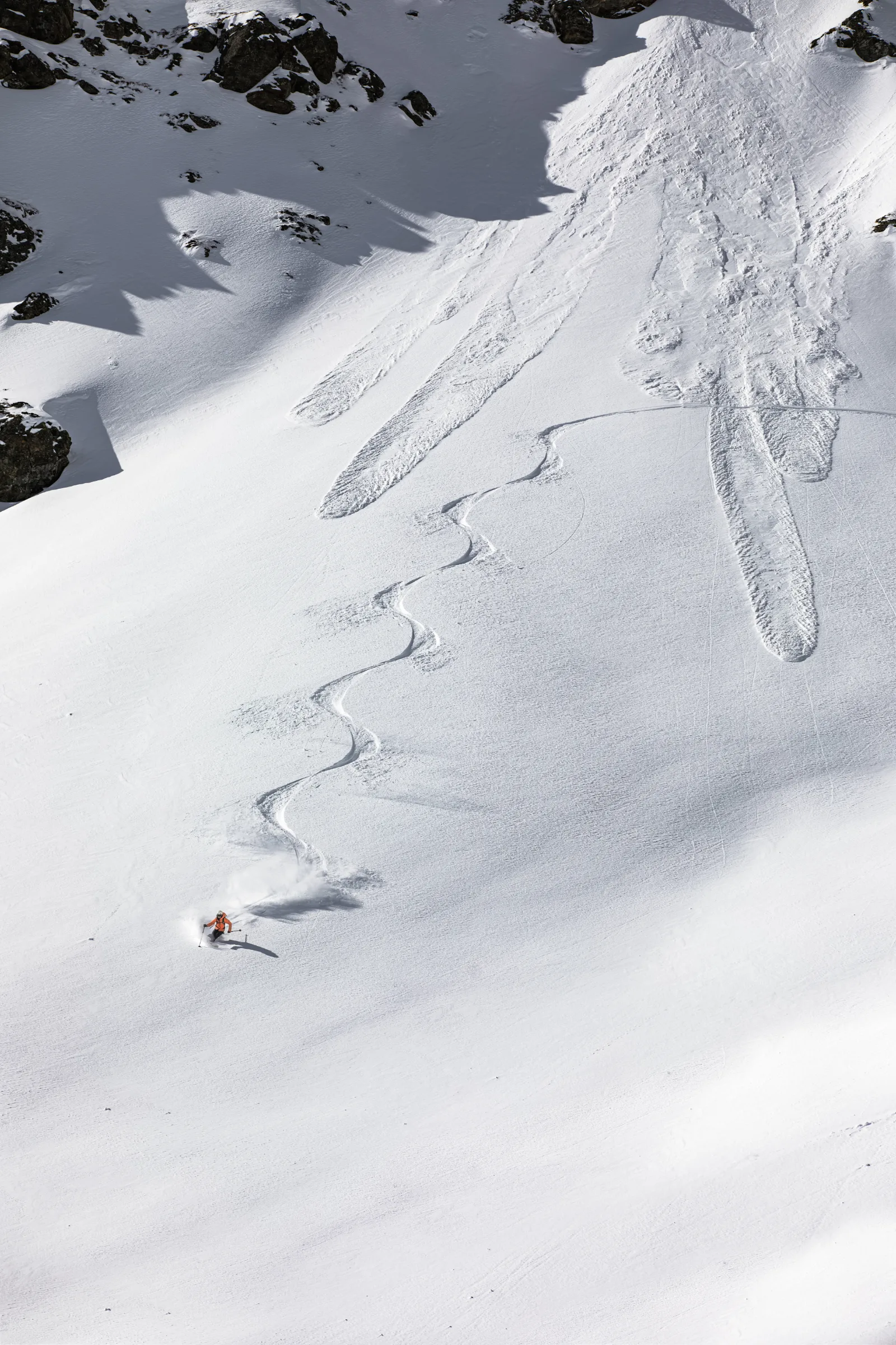 Mike Perl fährt unterhalb dunkler Felsen über einen weiten Schneehang in Lenzerheide; eine lange Folge geschwungener Skispuren liegt hinter ihm.
