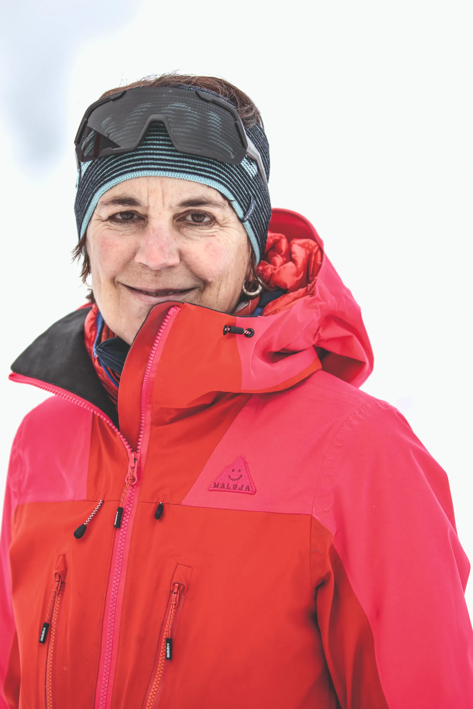 Petra Rapp lächelt vor hellem Hintergrund in die Kamera, trägt eine pink-rote Jacke und ein gestreiftes Stirnband mit darauf geschobener Sonnenbrille.