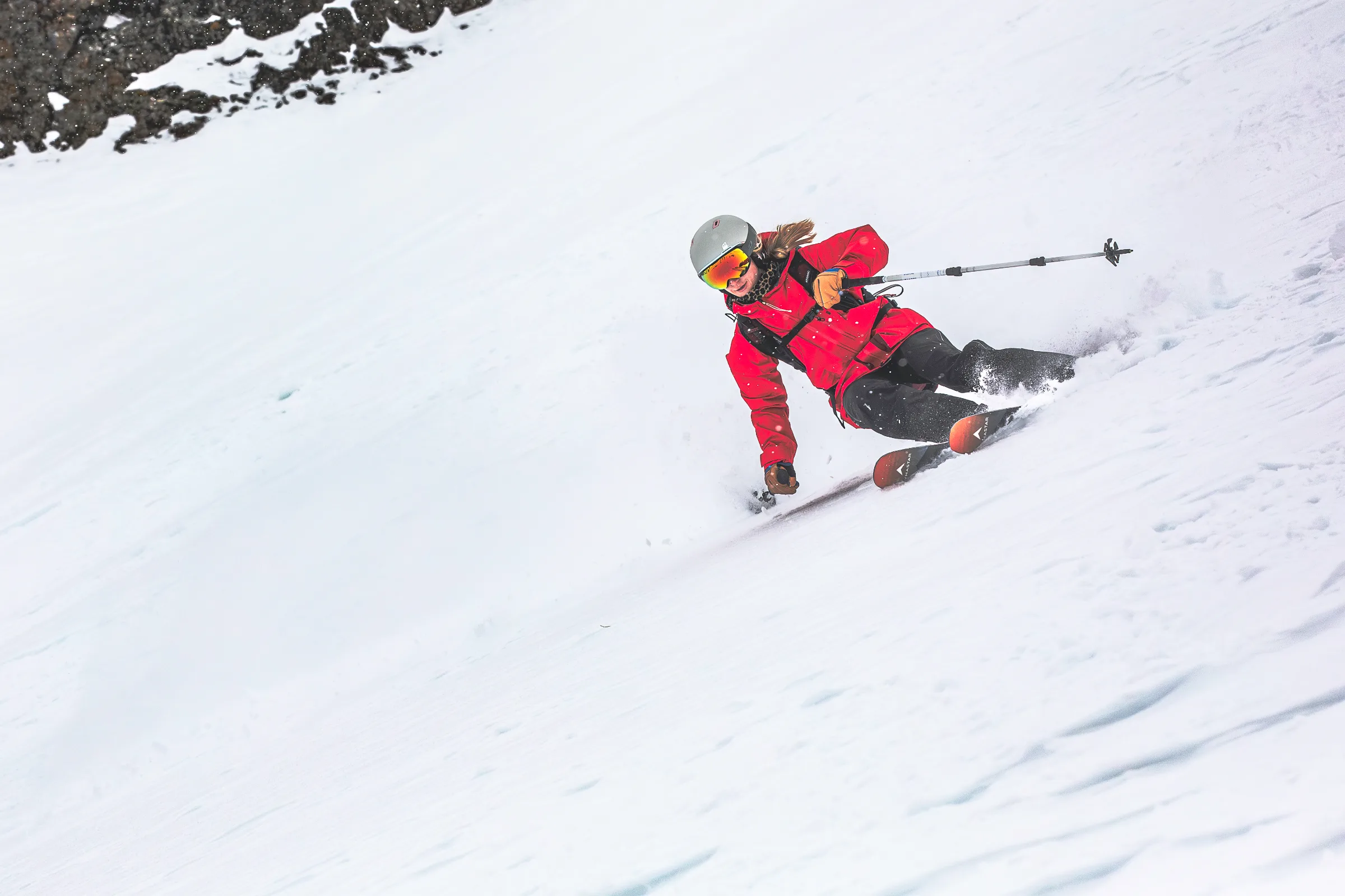 Pia Vogt leans deeply into a turn on a steep snowy slope, with one hand close to the snow and a ski pole extended sideways.