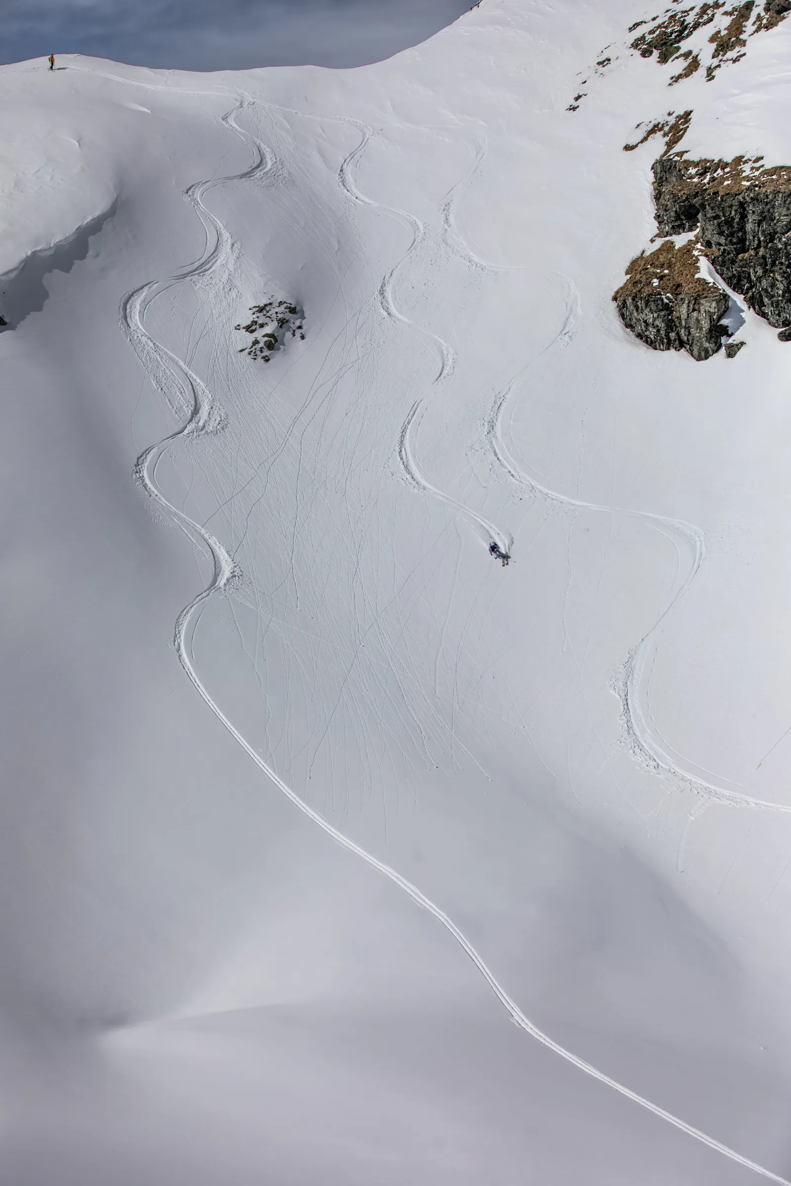 Pia Vogt makes a turn through the snow below a rock face, with long S-shaped ski tracks winding down the broad slope in Lenzerheide.