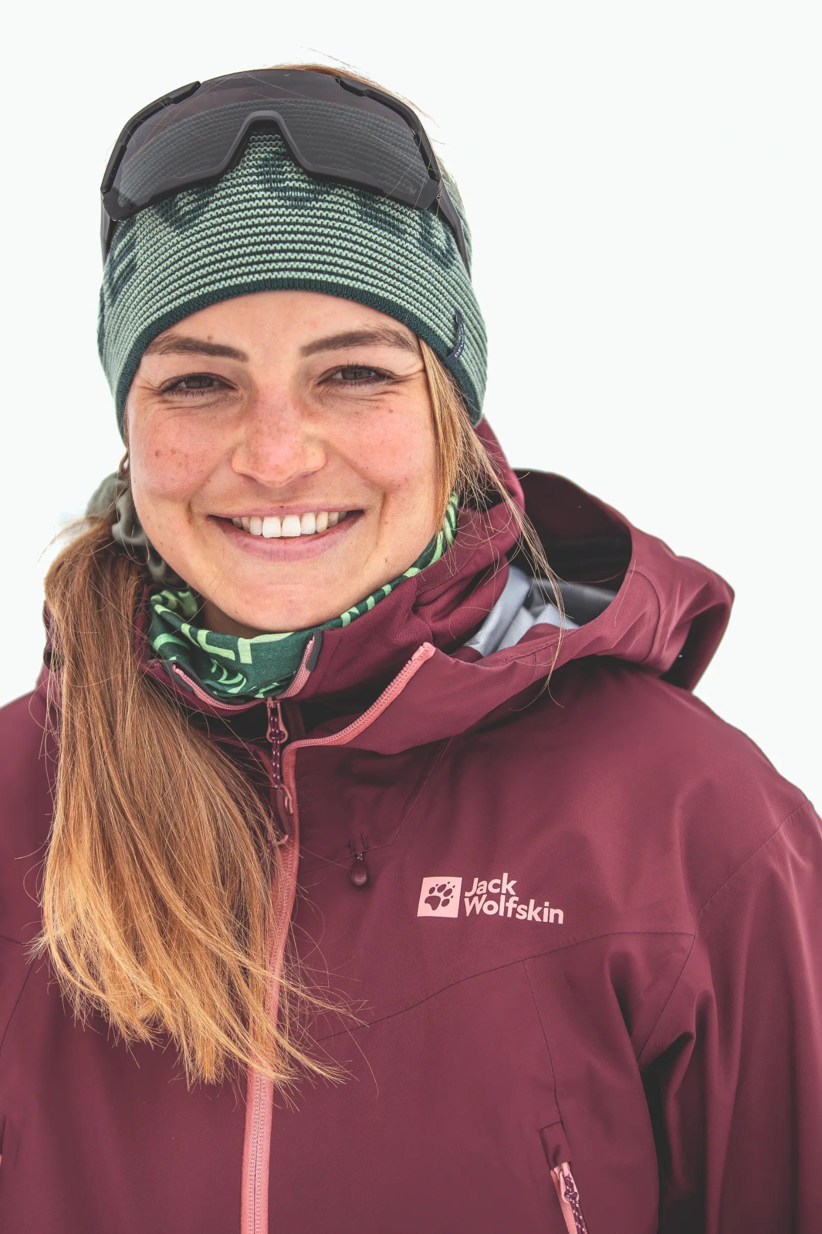 Ramona Arendt smiles at the camera against a white background, wearing a green headband with sunglasses pushed up on it and a burgundy jacket.