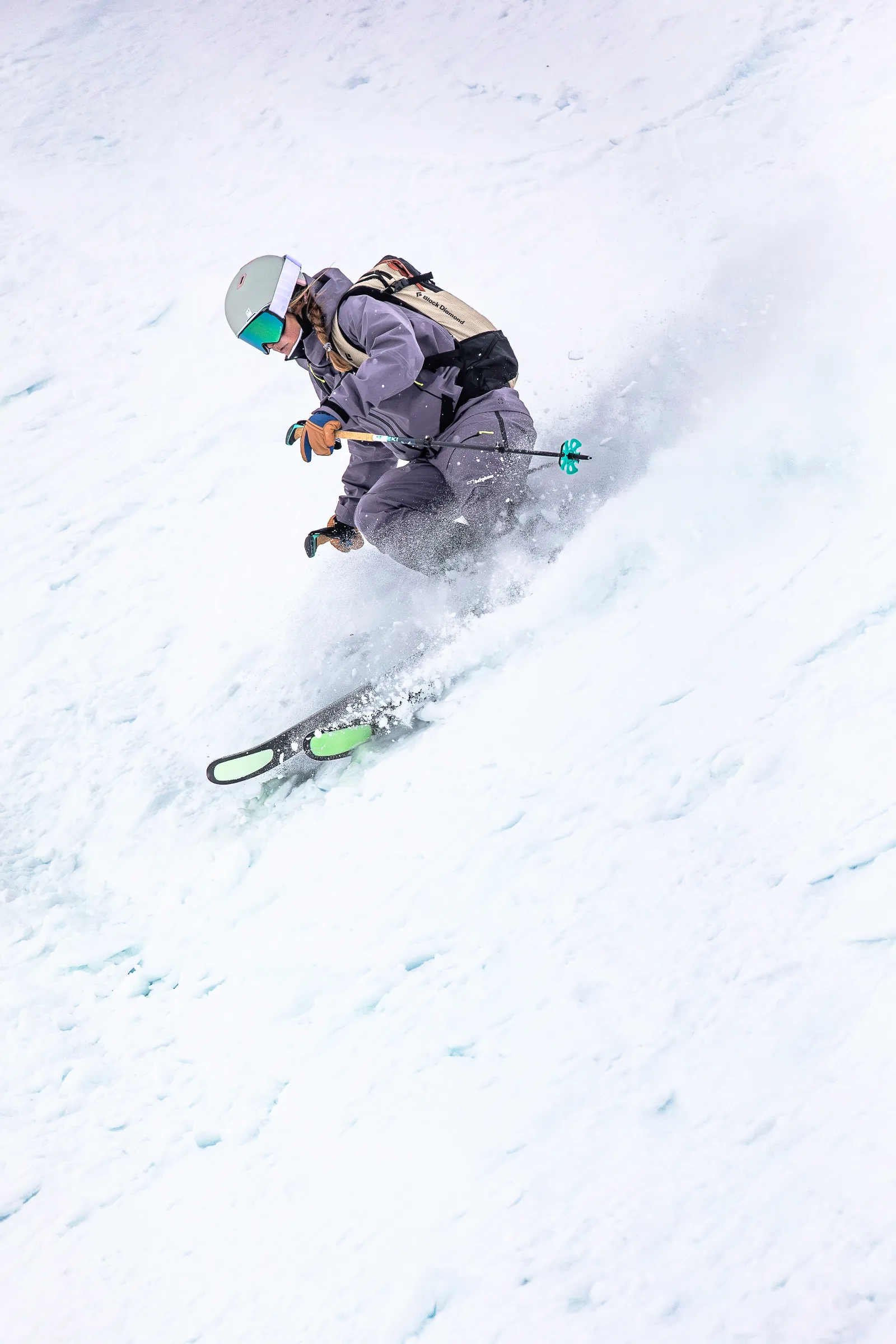Ramona Arendt crouches low in purple ski clothing as she turns through the snow, throwing up spray beside her skis.