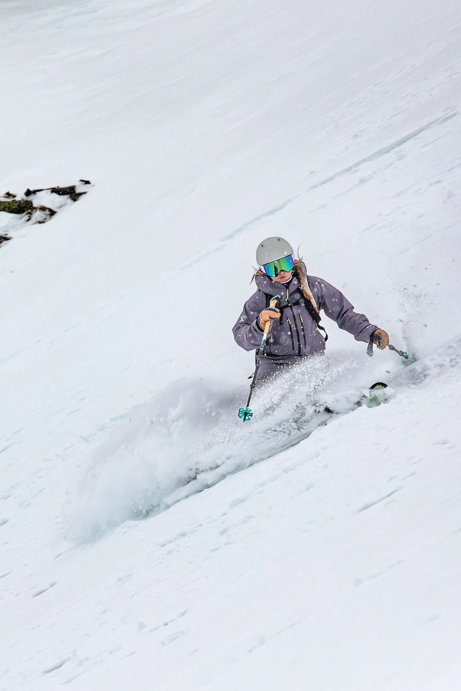 Ramona Arendt, wearing a helmet and mirrored goggles, turns down a snowy slope as snow sprays up in front of her knees.