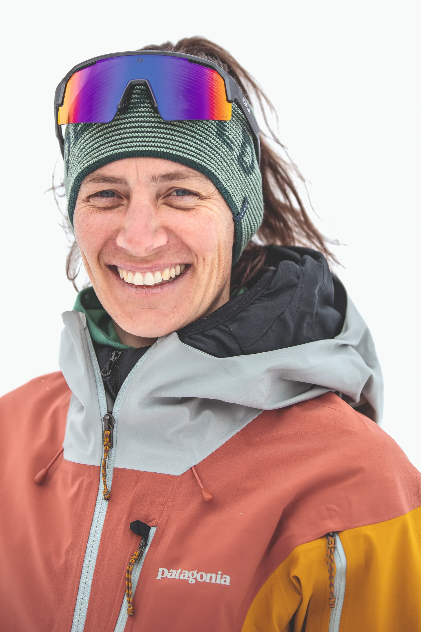Sabine Speidel smiles in close-up against a white background, wearing a green knitted headband with mirrored sports sunglasses resting on her forehead.