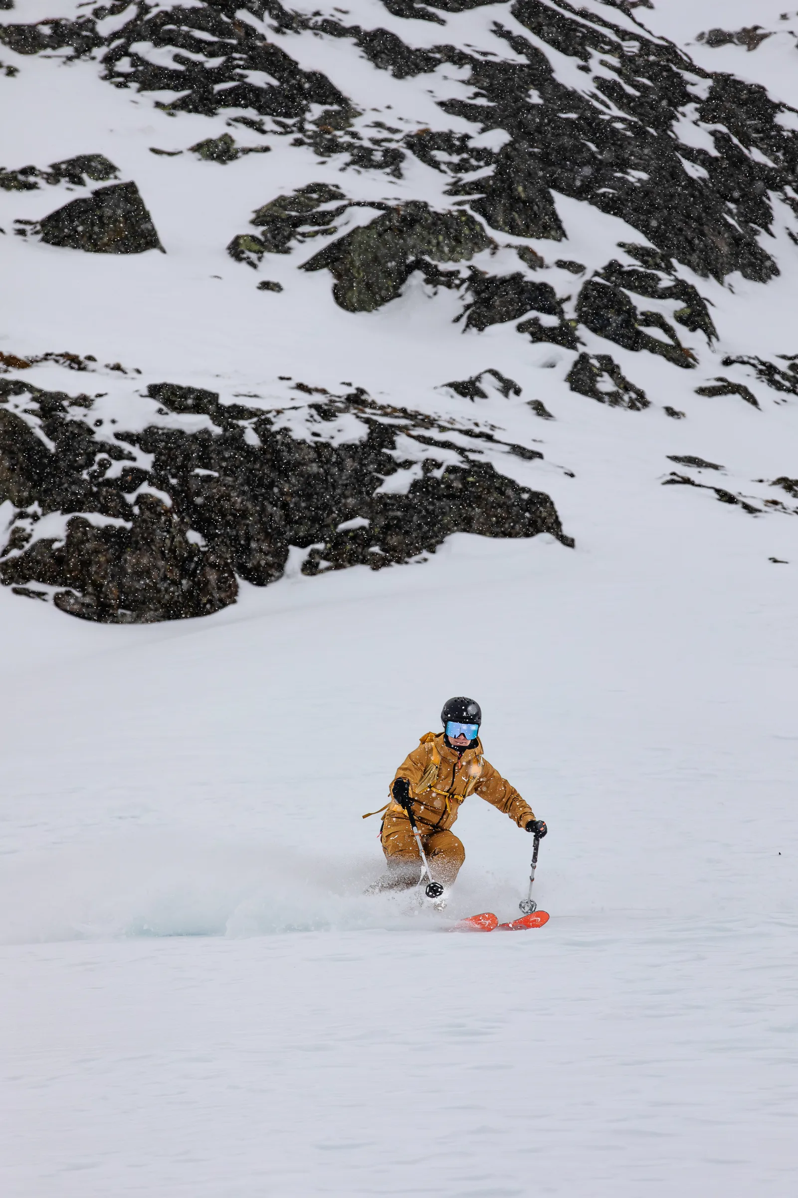 Sabine Speidel turns below dark rocks in falling snow, her red ski tips throwing up powder.
