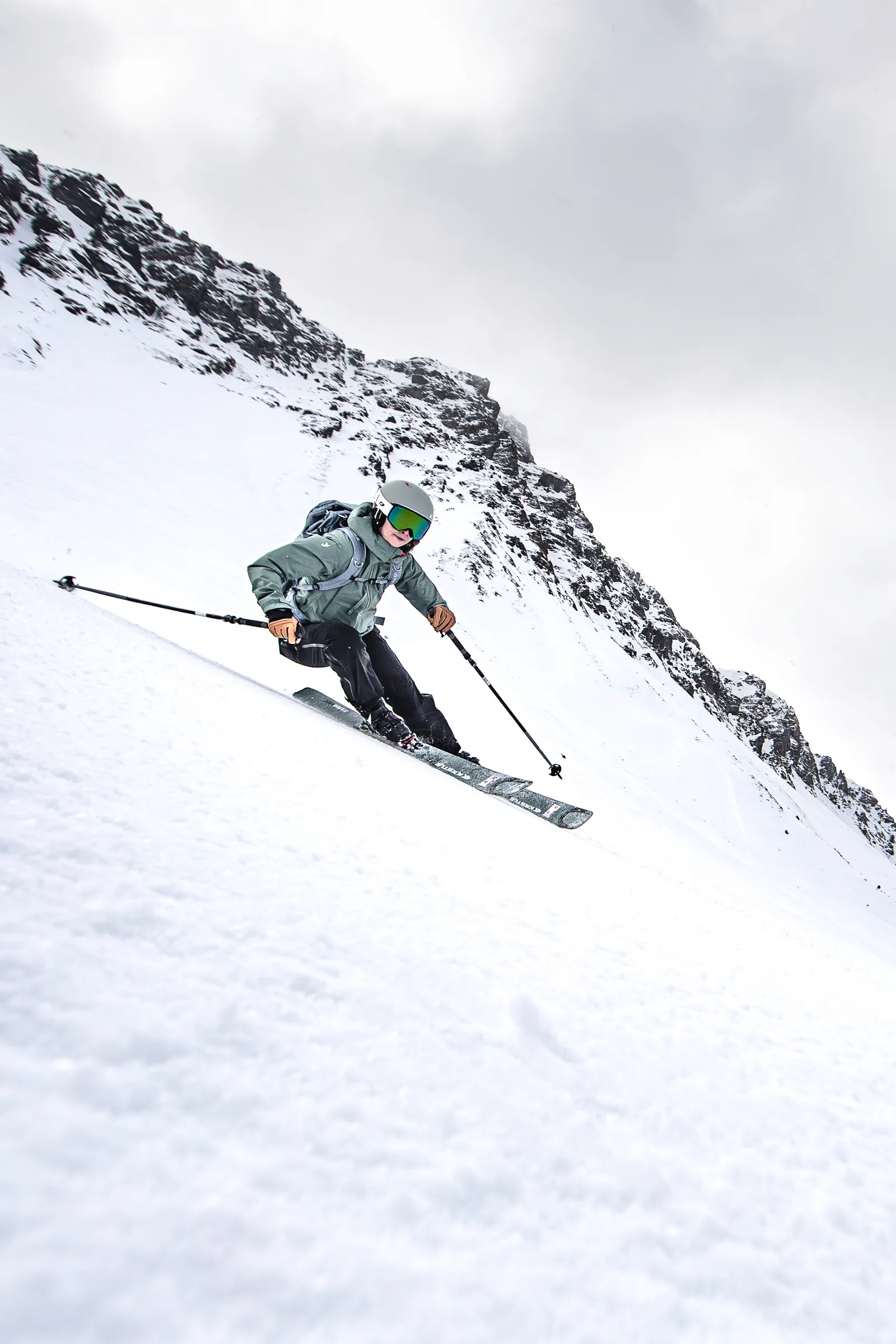 Sabrina Stickl legt sich mit tief gebeugten Knien in einen Schwung auf einem steilen Schneehang unterhalb dunkler Felsen.