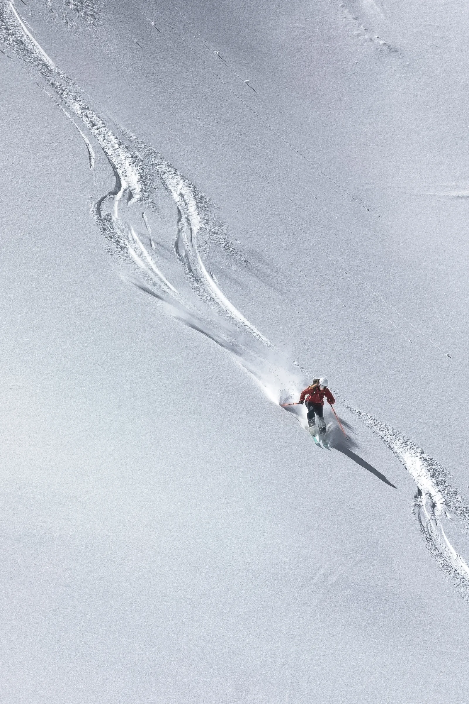 Sabrina Stickl fährt in roter Jacke und weißem Helm durch den Tiefschnee; hinter ihr ziehen sich geschwungene Skispuren und eine Schneefahne über den Hang.