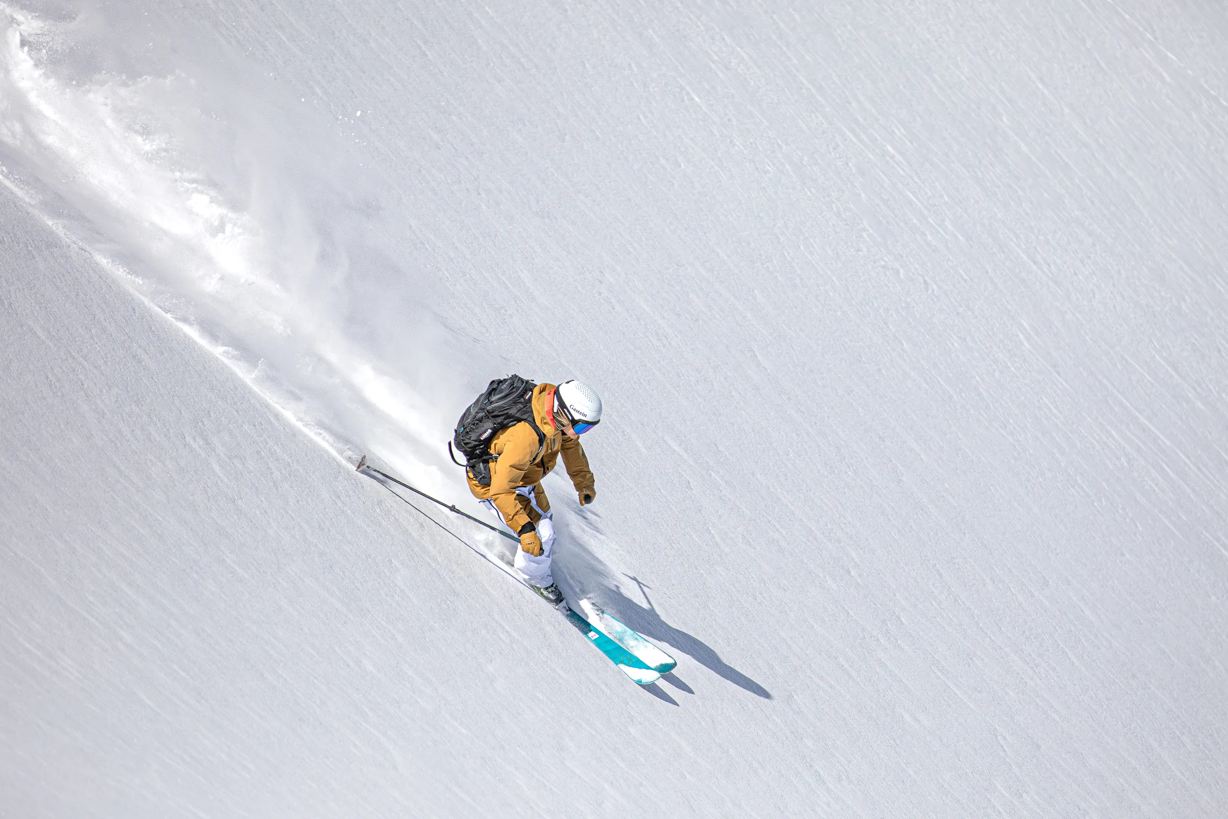 Von oben gesehen fährt Sandra Lahnsteiner-Wagner mit schwarzem Rucksack und türkisfarbenen Ski durch frischen Schnee und hinterlässt eine geschwungene Spur.