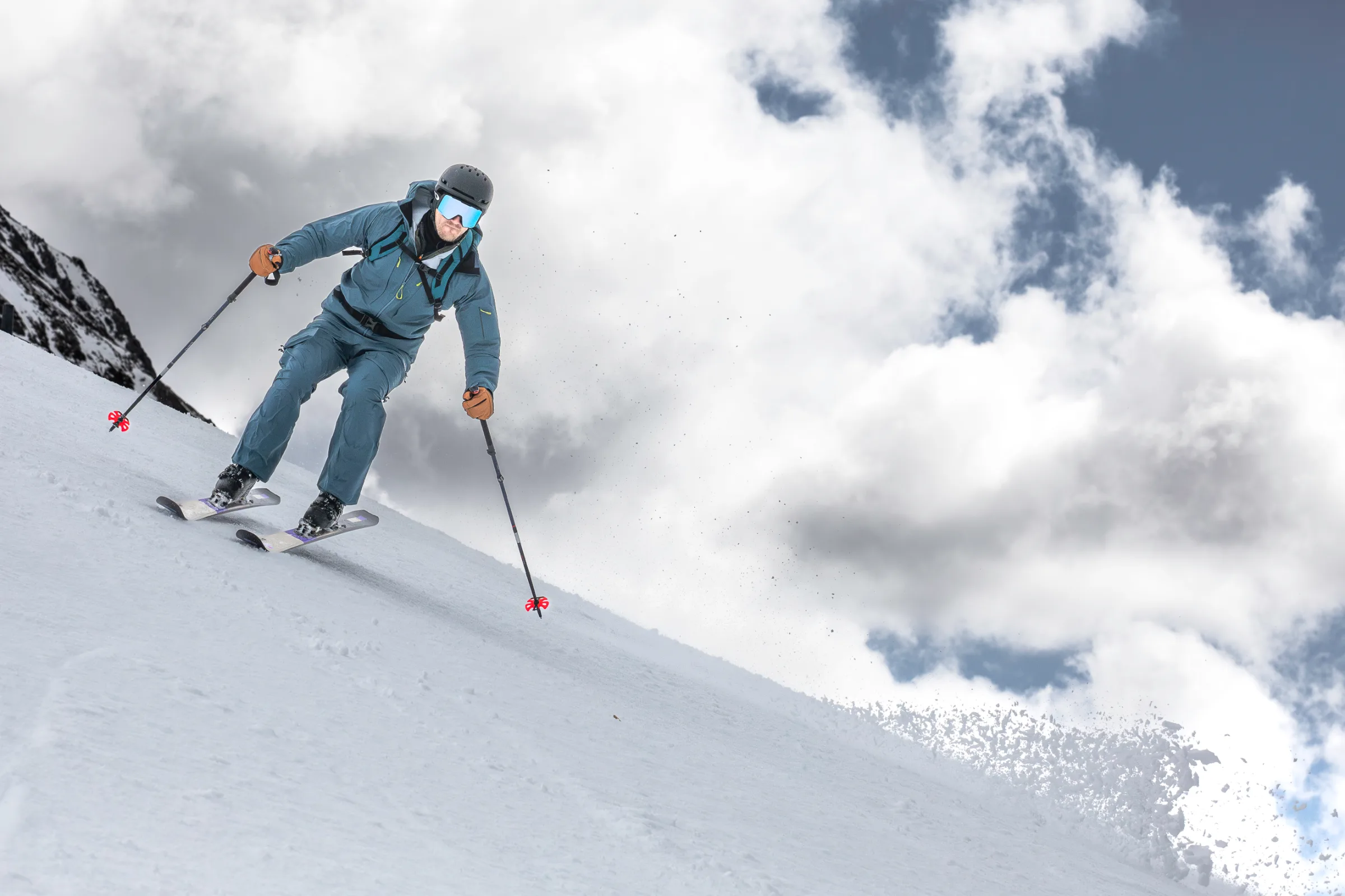 Simon Stickl skis down a snowy slope in Lenzerheide in blue ski clothing, a helmet and backpack, beneath large clouds.