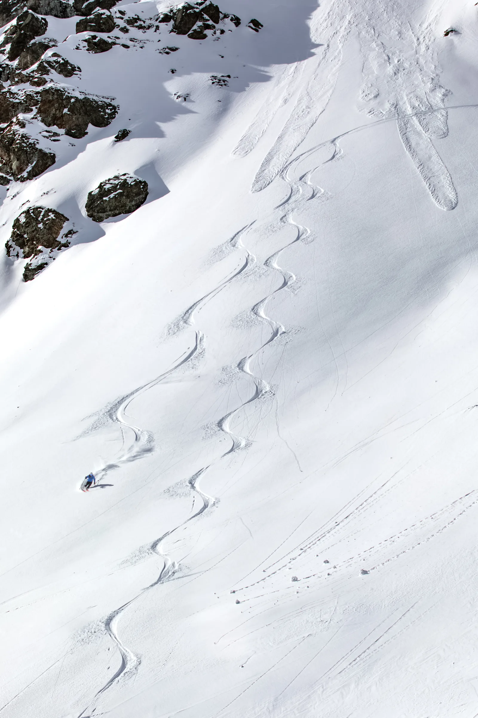 Simon Stickl makes a turn on a broad snowy slope in Lenzerheide, with long winding ski tracks and dark rocks stretching above him.
