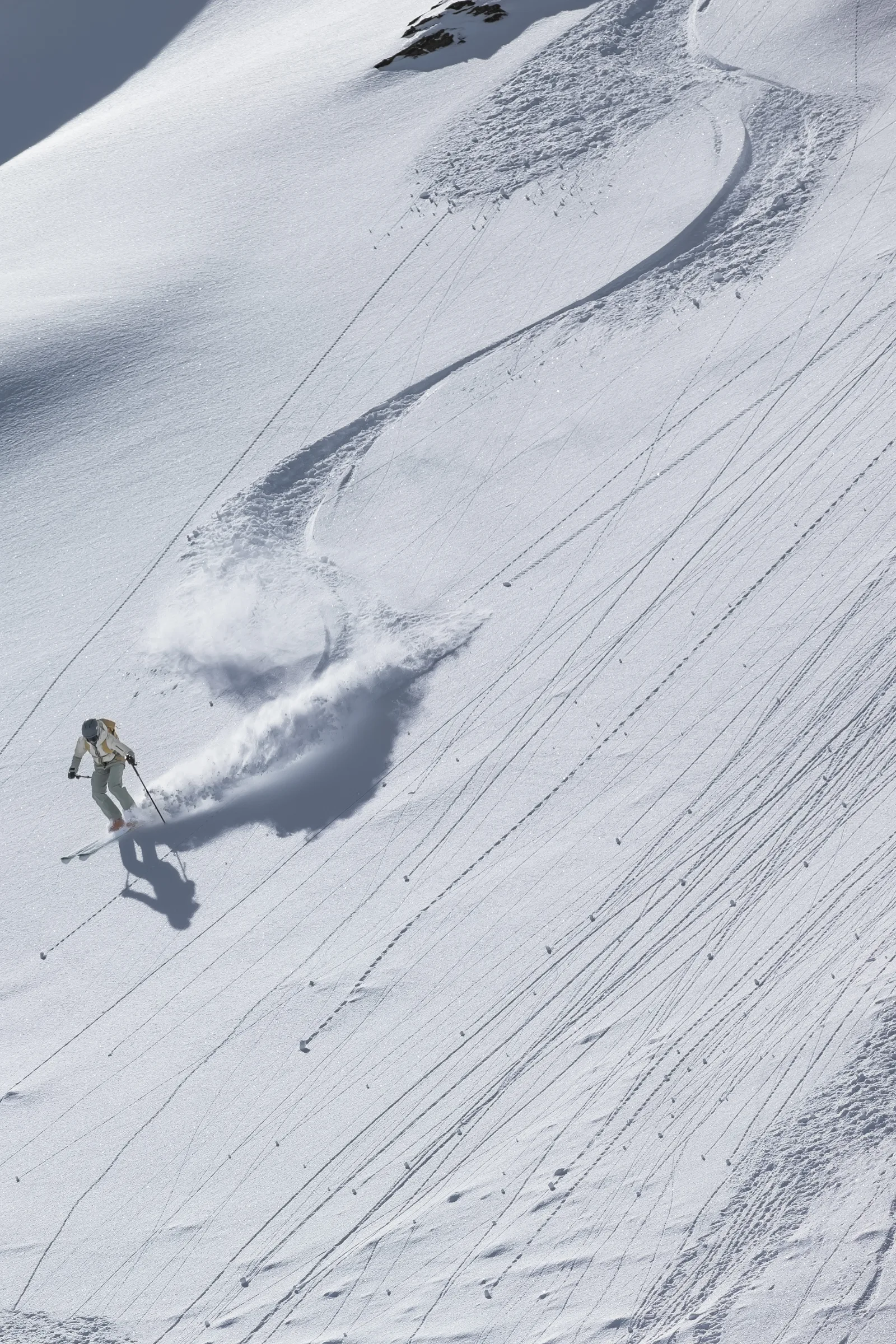 Sofia Muigg skis left through powder, leaving a winding track and a broad plume of snow across the slope behind her.