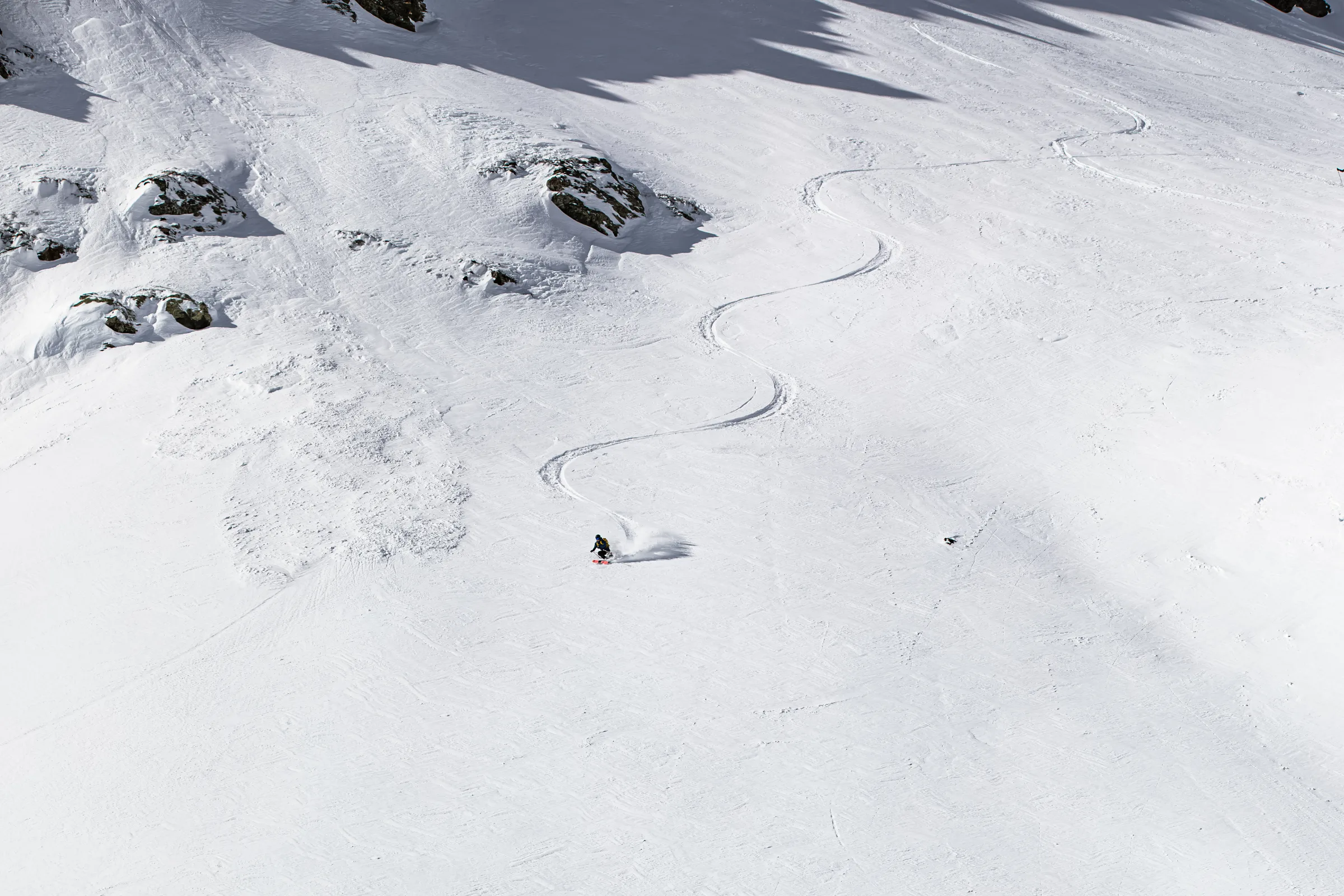 Valentin Rapp makes a turn on a broad snowy slope in Lenzerheide, with his long S-shaped track winding uphill between scattered rocks.